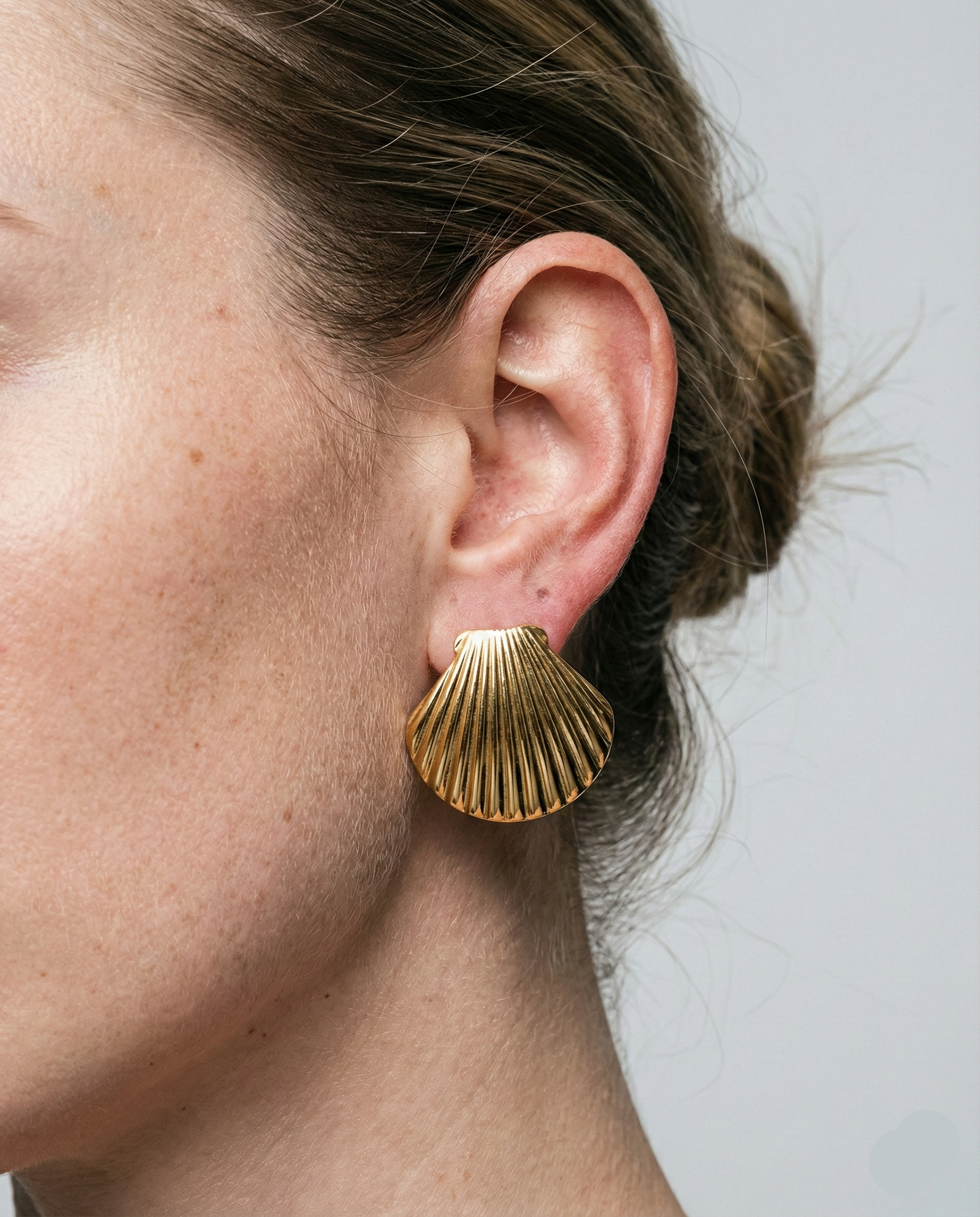 Gold shell-shaped earring worn by a person on a neutral background