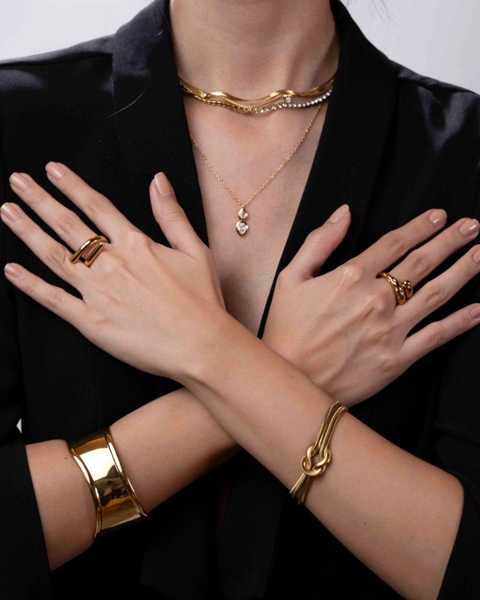 Gold jewelry including bracelets, necklaces, and rings on a person wearing a black outfit.