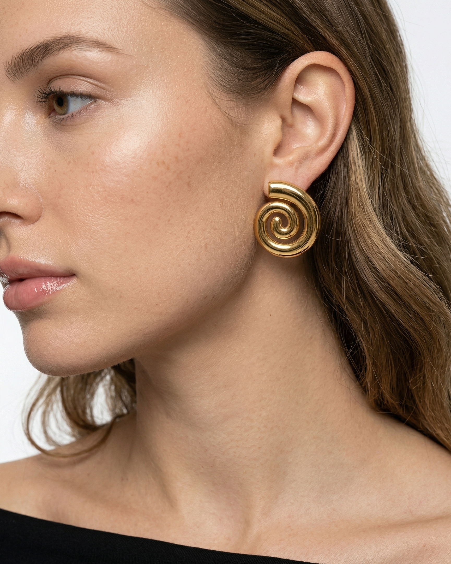 Close-up of a woman wearing gold spiral earrings with a plain background