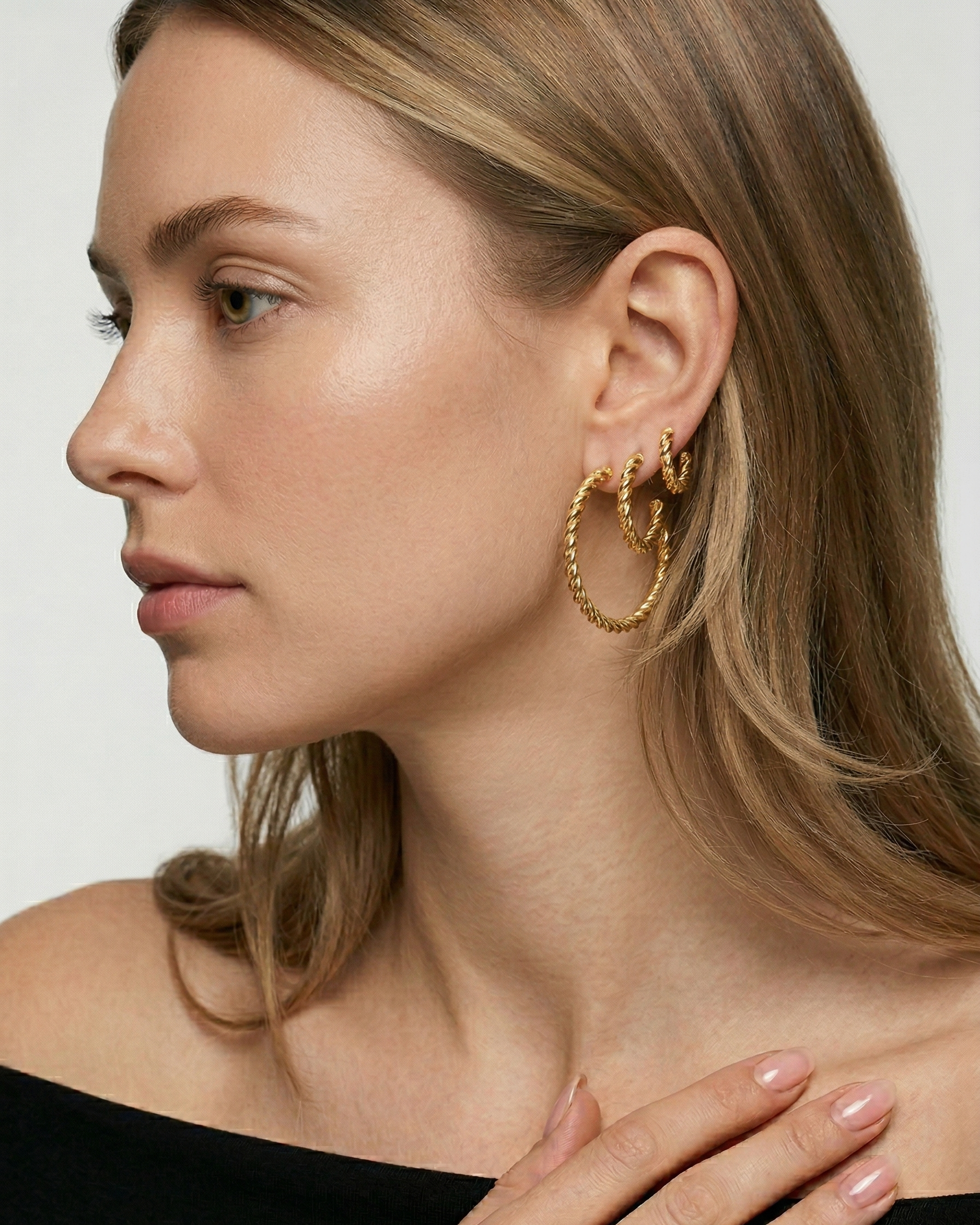 Close-up of a woman wearing gold hoop earrings with a neutral background