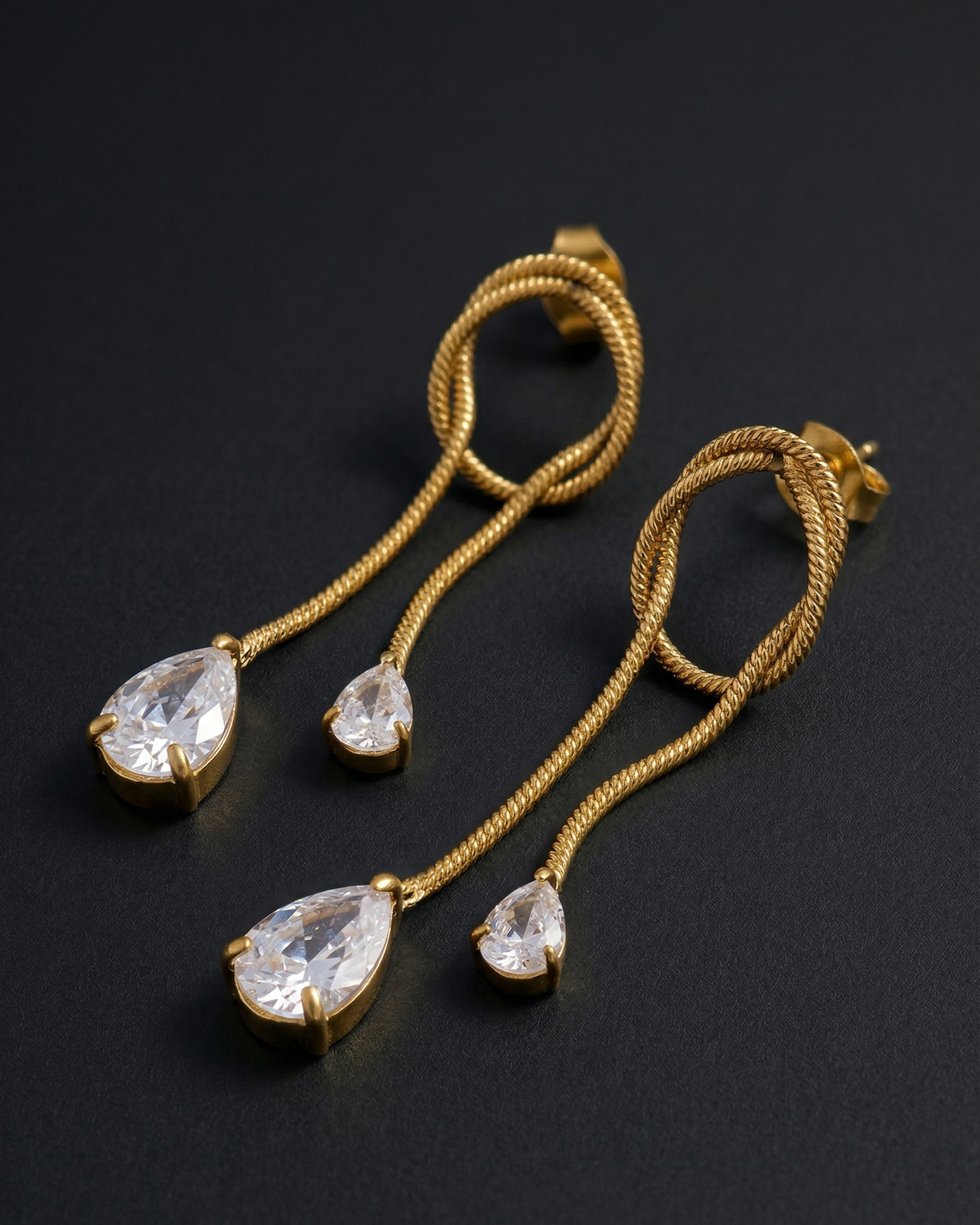 Gold earrings with teardrop-shaped crystals on a dark background