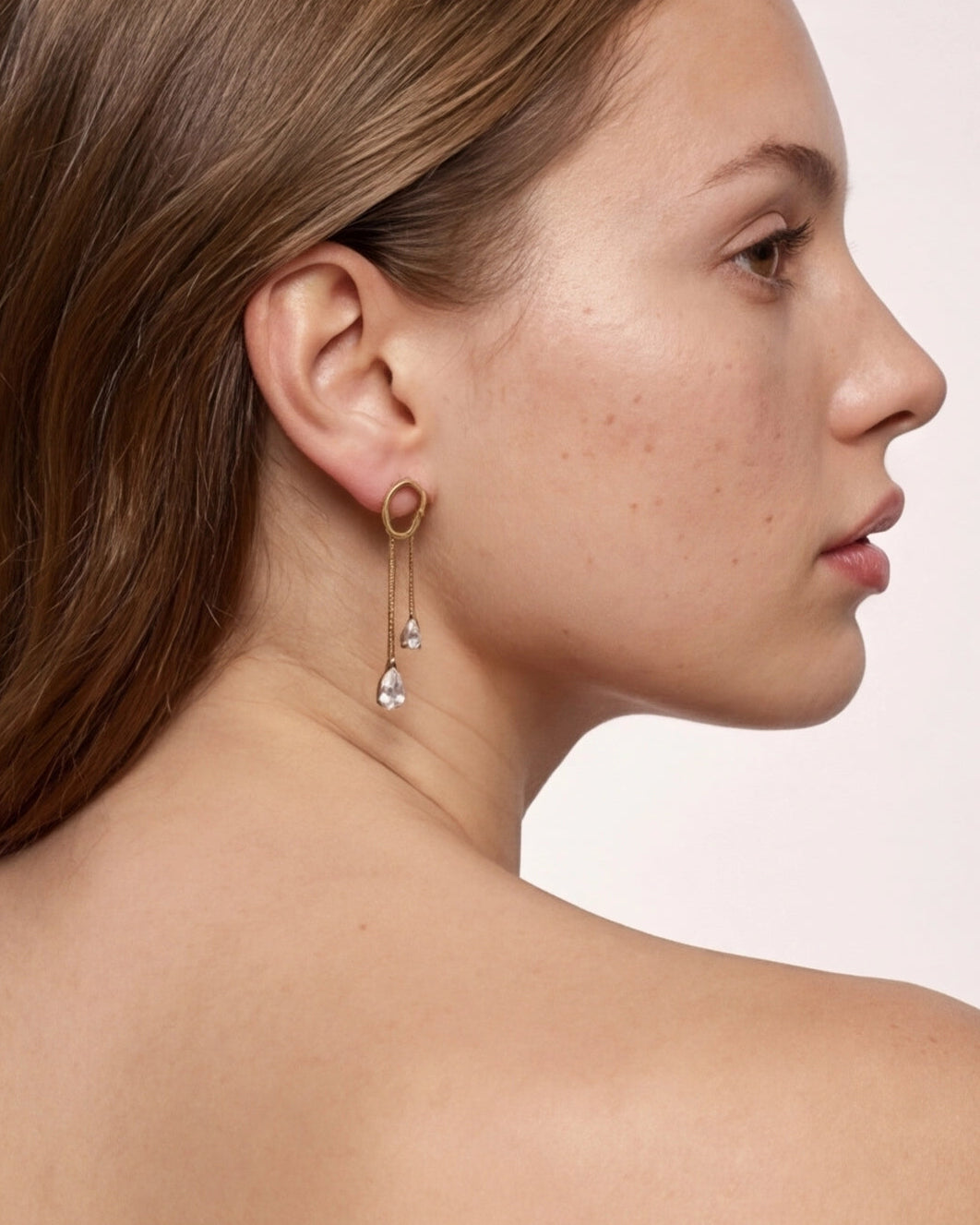 Close-up of a woman wearing a gold earring with dangling elements on a plain background