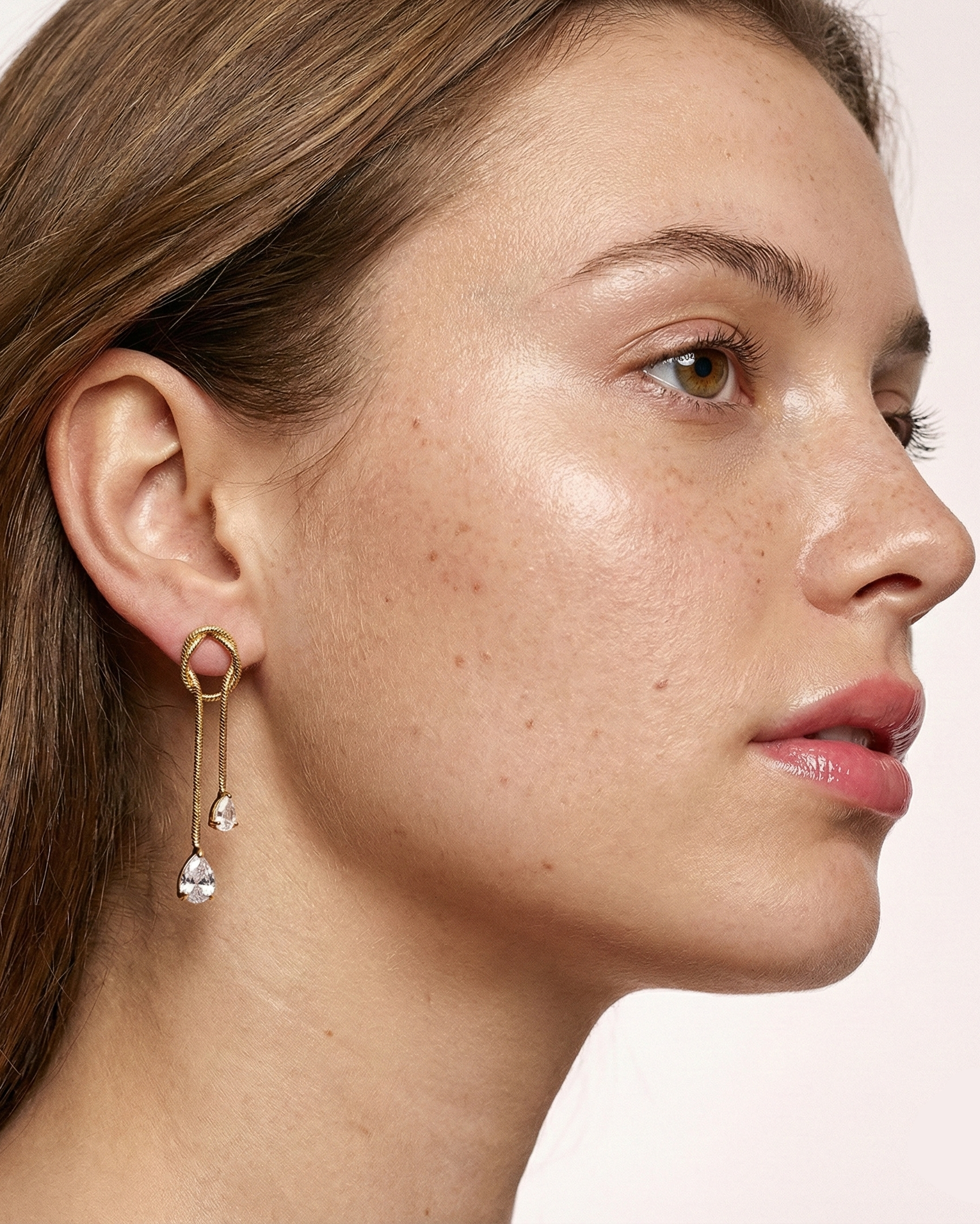 Close-up of a woman wearing a gold earring with dangling elements on a plain background