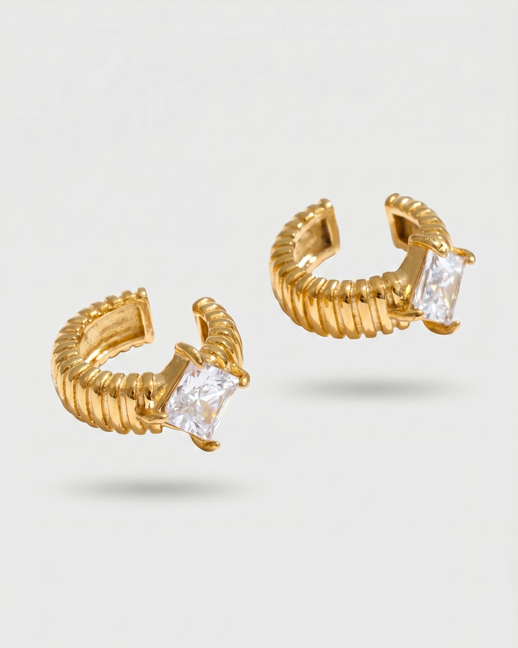 Gold hoop earrings with clear gemstones on a light gray background