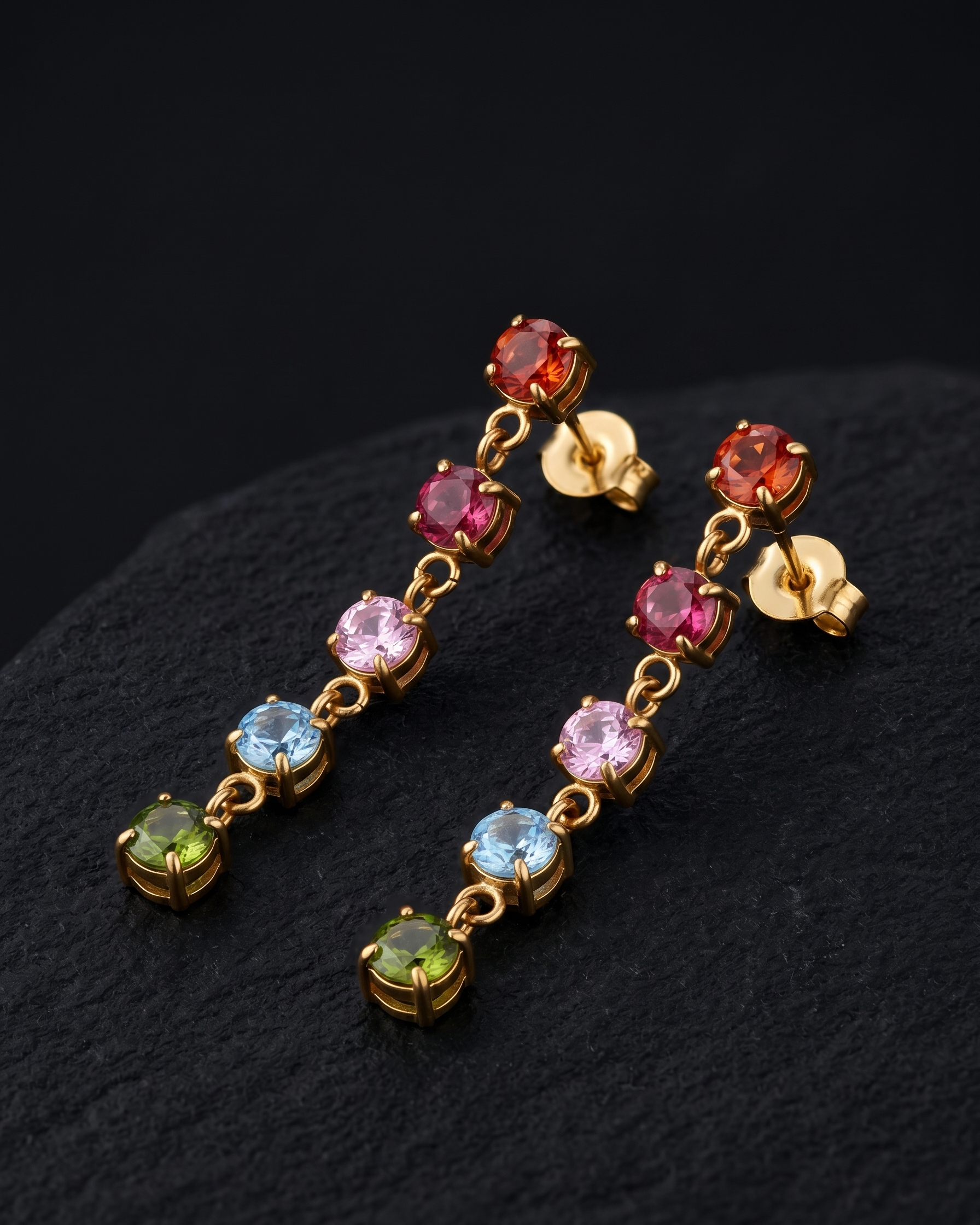 Pair of gold earrings with multicolored gemstones on a dark background
