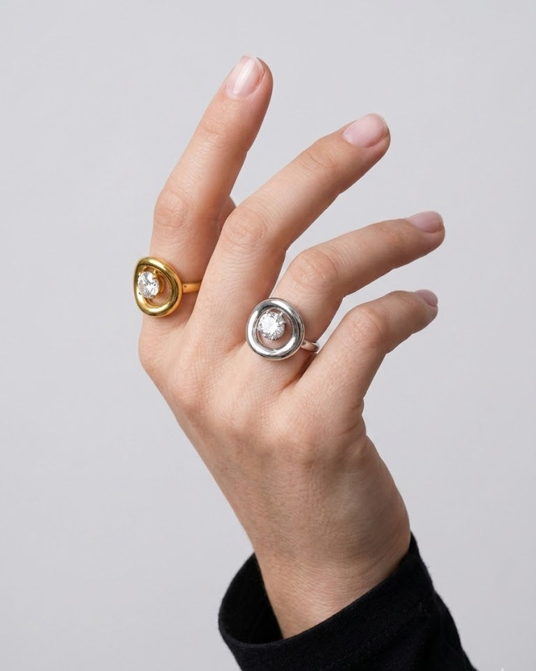Hand wearing two rings with gold and silver bands on a plain background