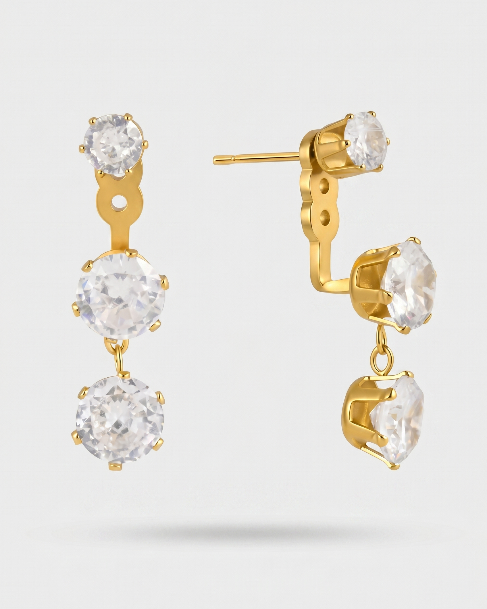 Gold earrings with clear gemstones on a light gray background
