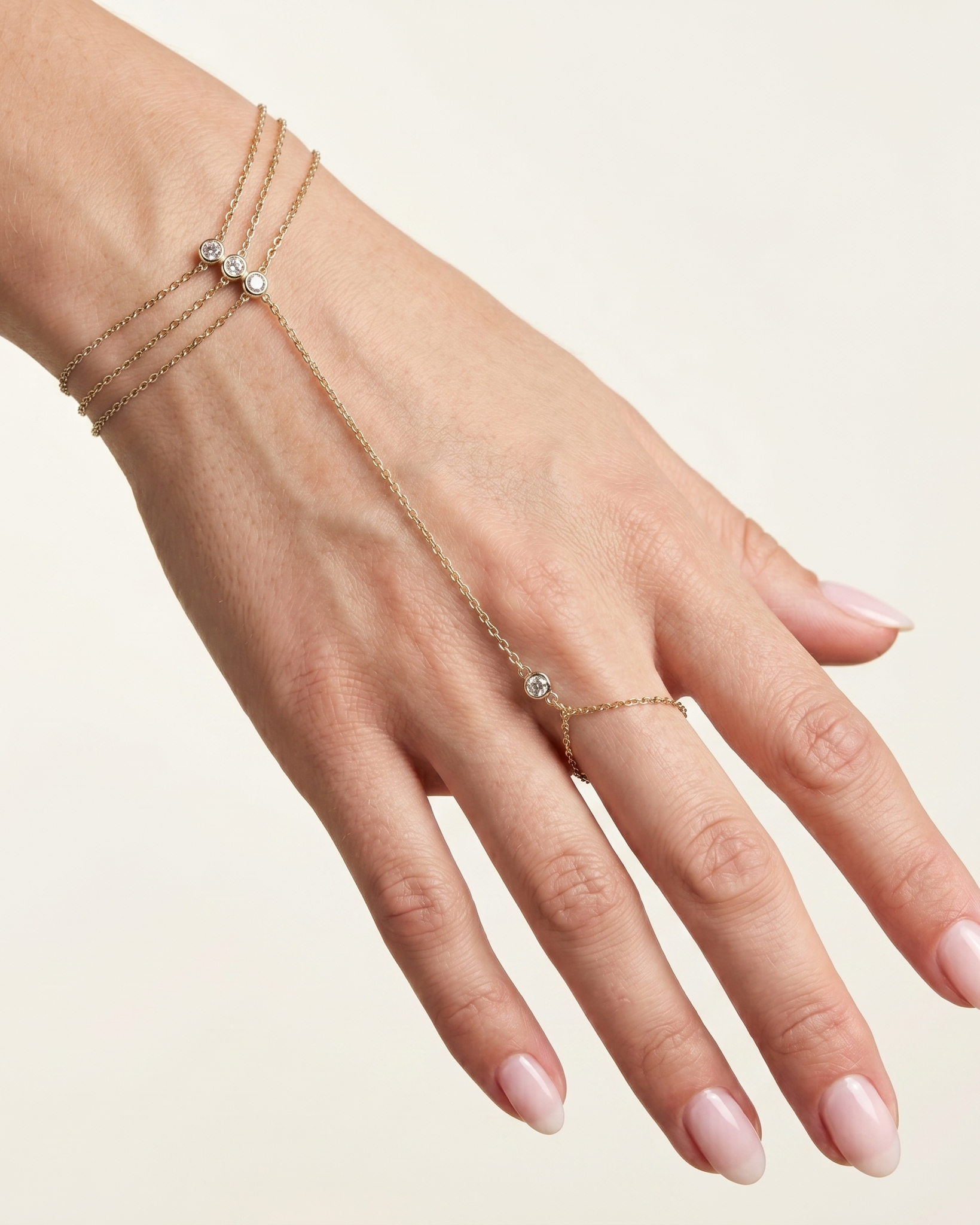 Hand wearing a delicate gold bracelet with small stones on a light background