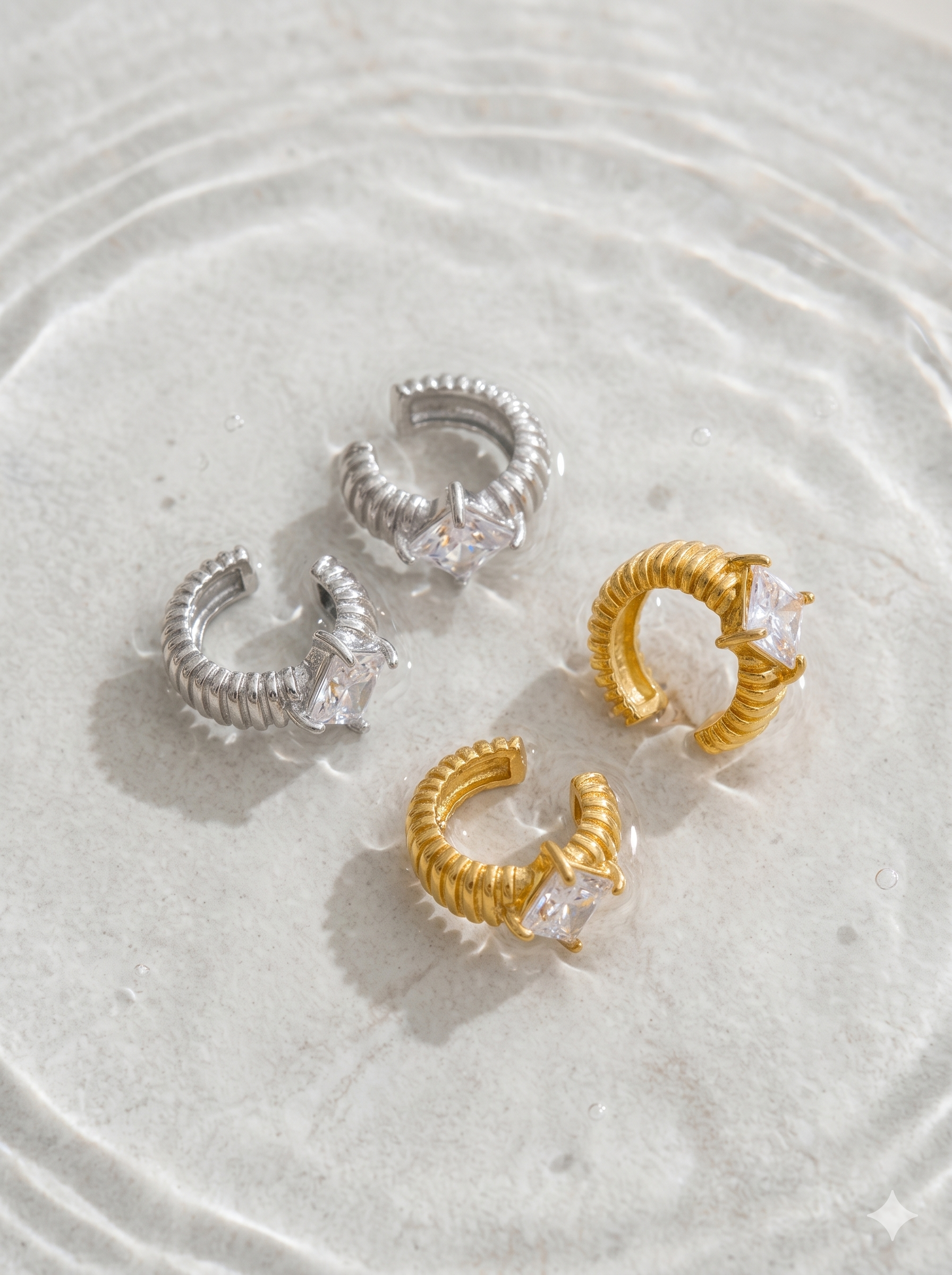 Pair of gold and silver hoop earrings with clear gemstones on a textured white surface.
