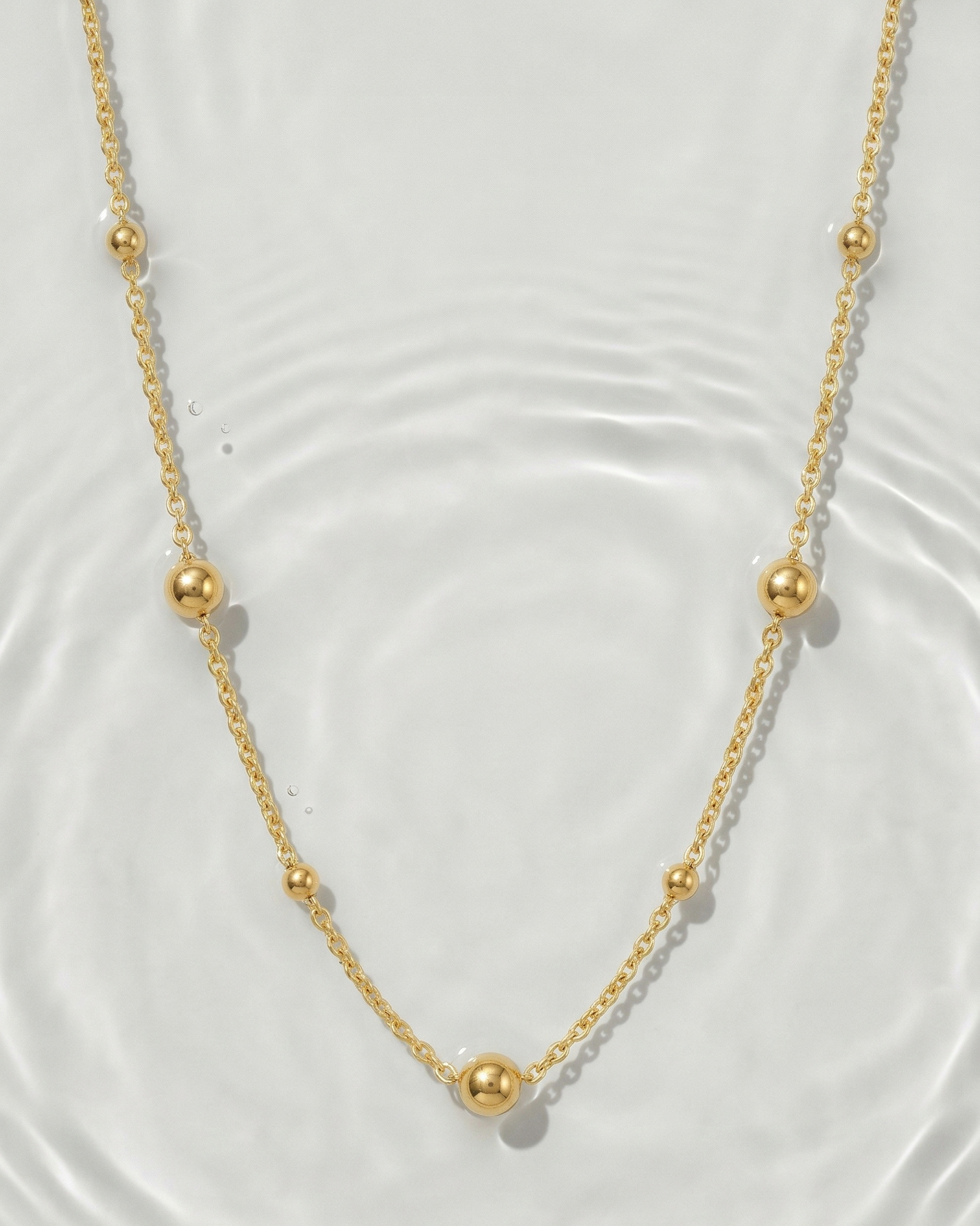 Gold necklace with small beads on a white background
