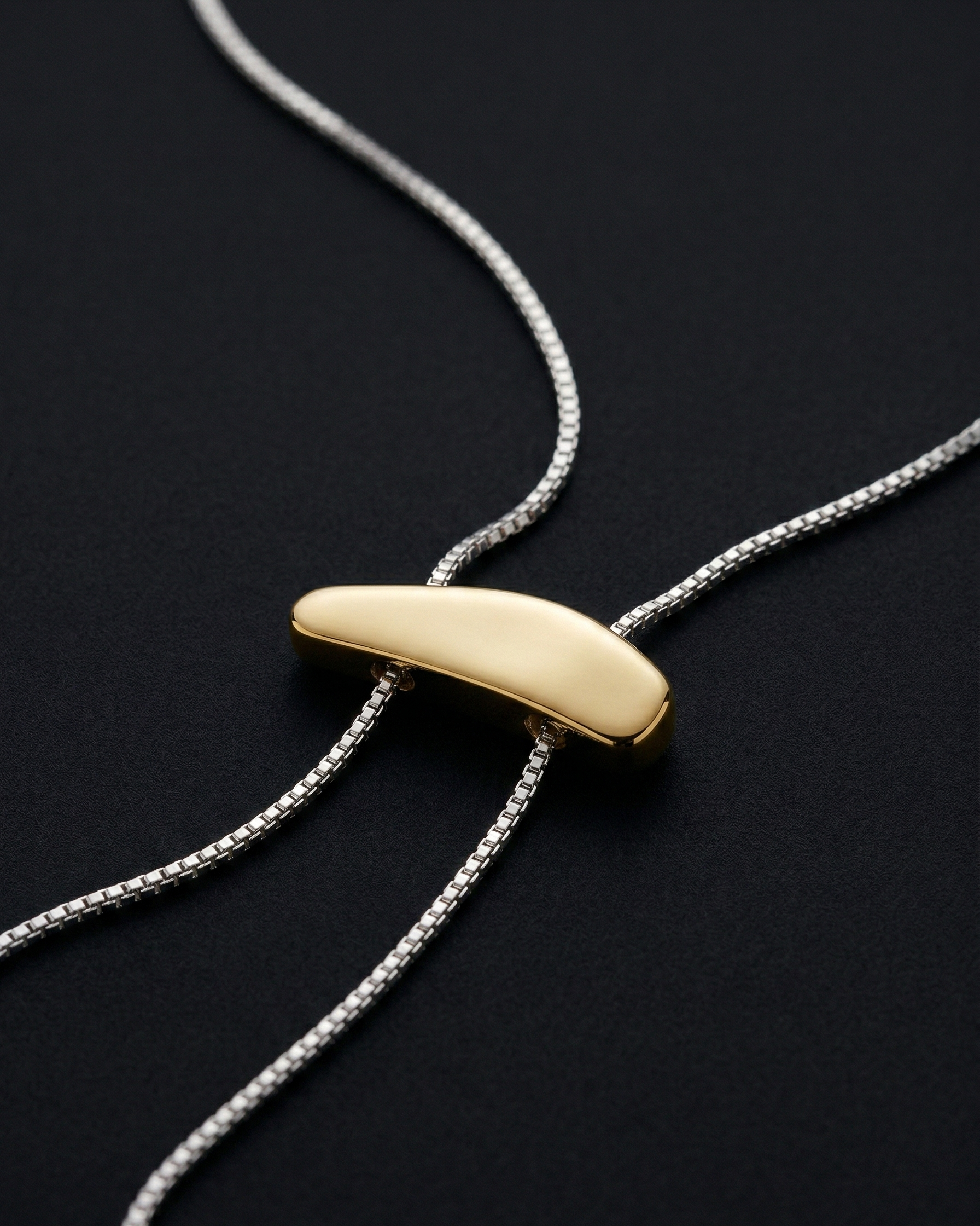 Gold pendant on a silver chain against a black background