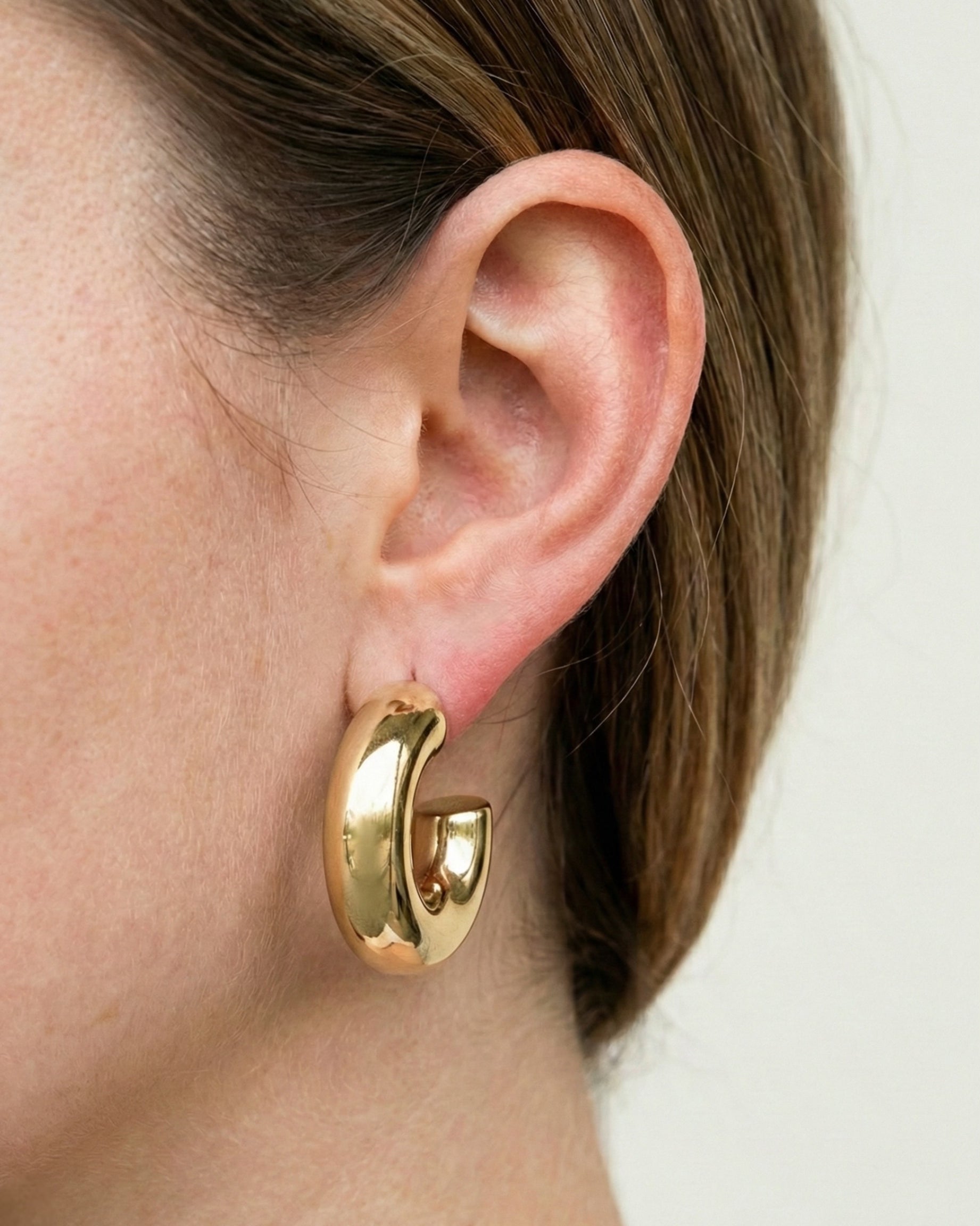 Gold hoop earring worn by a person with a neutral background