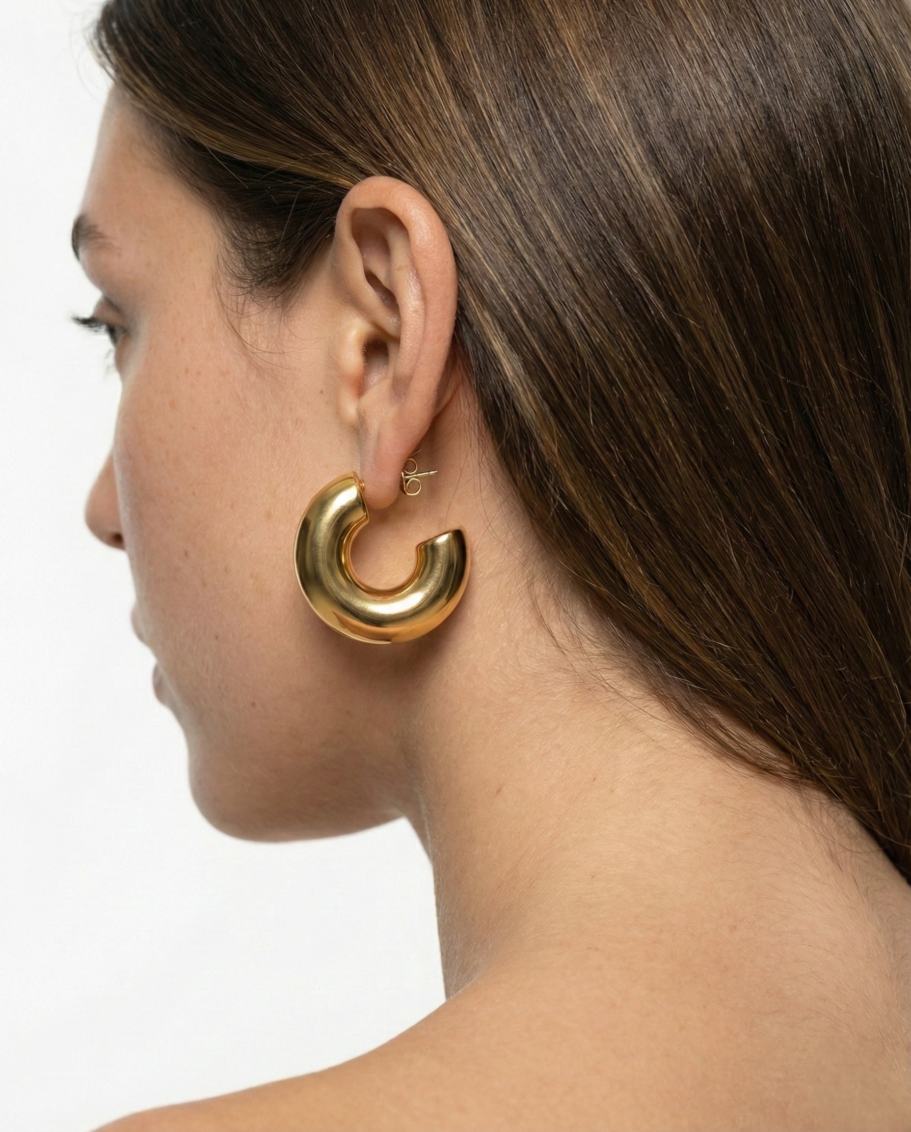 Gold hoop earring worn by a person with a neutral background