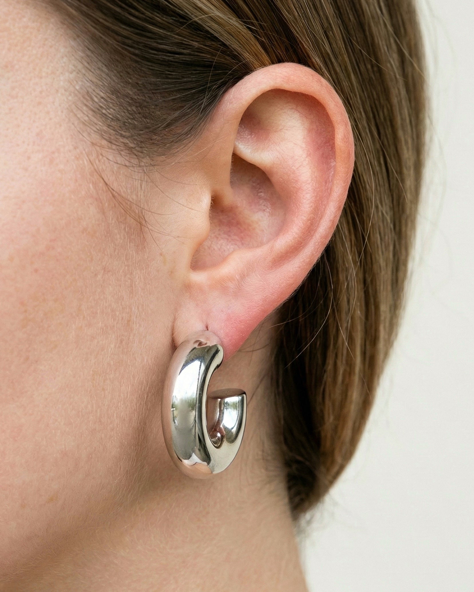 Silver hoop earring worn by a person with a neutral background