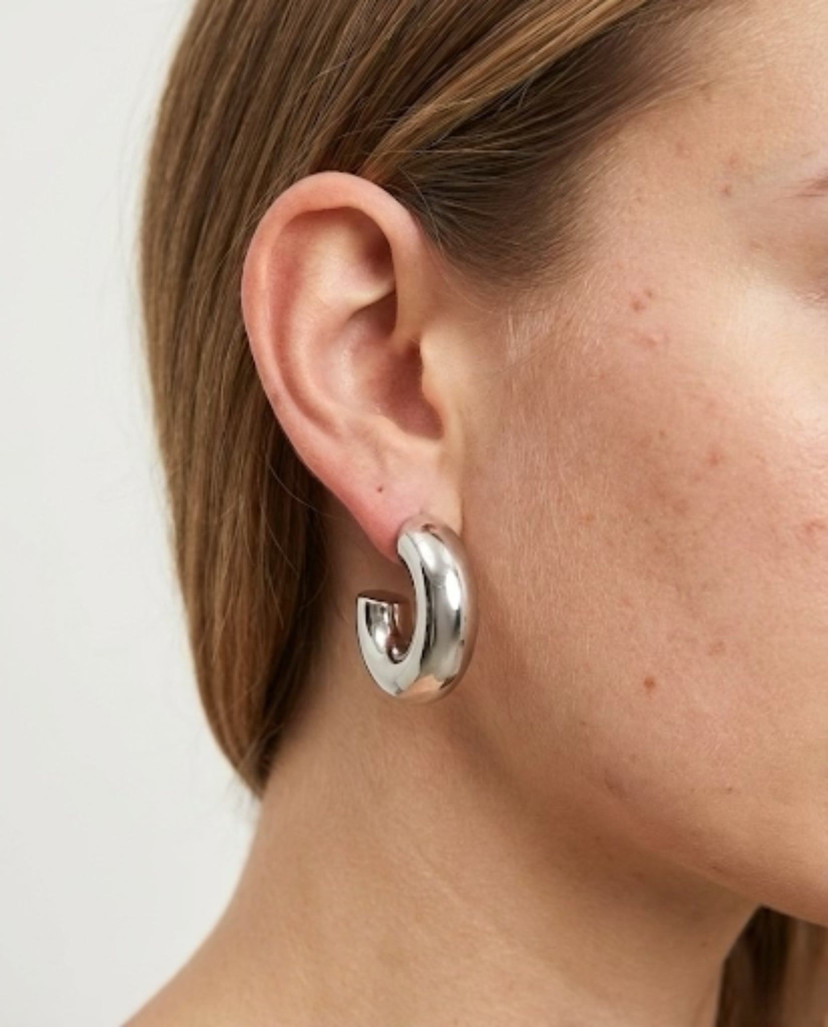 Silver hoop earring worn by a person on a plain background