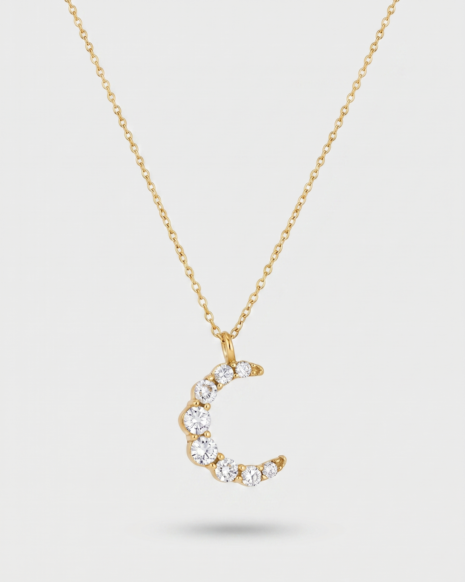 Gold necklace with a crescent moon pendant on a light gray background