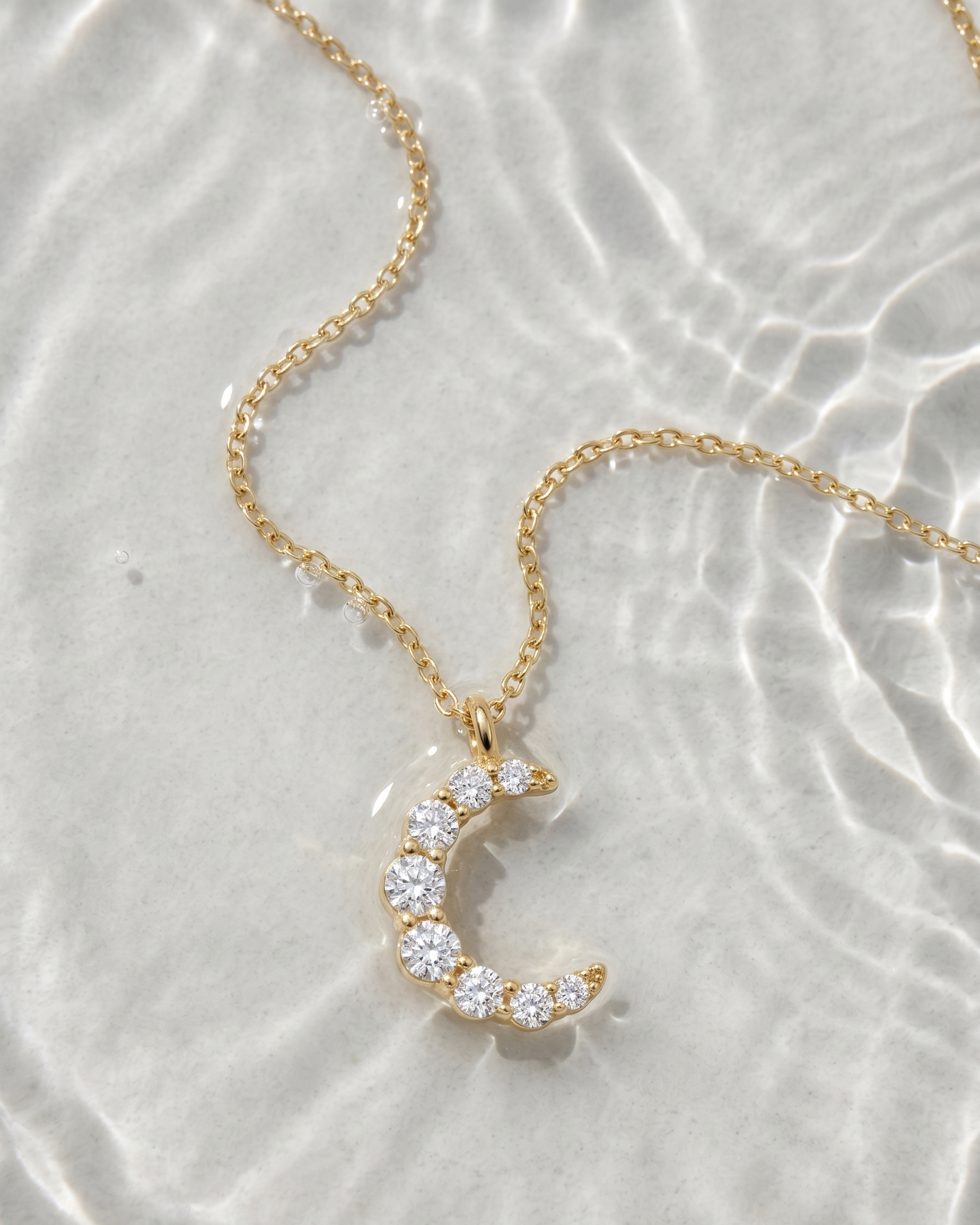 Gold necklace with a crescent moon pendant on a light background