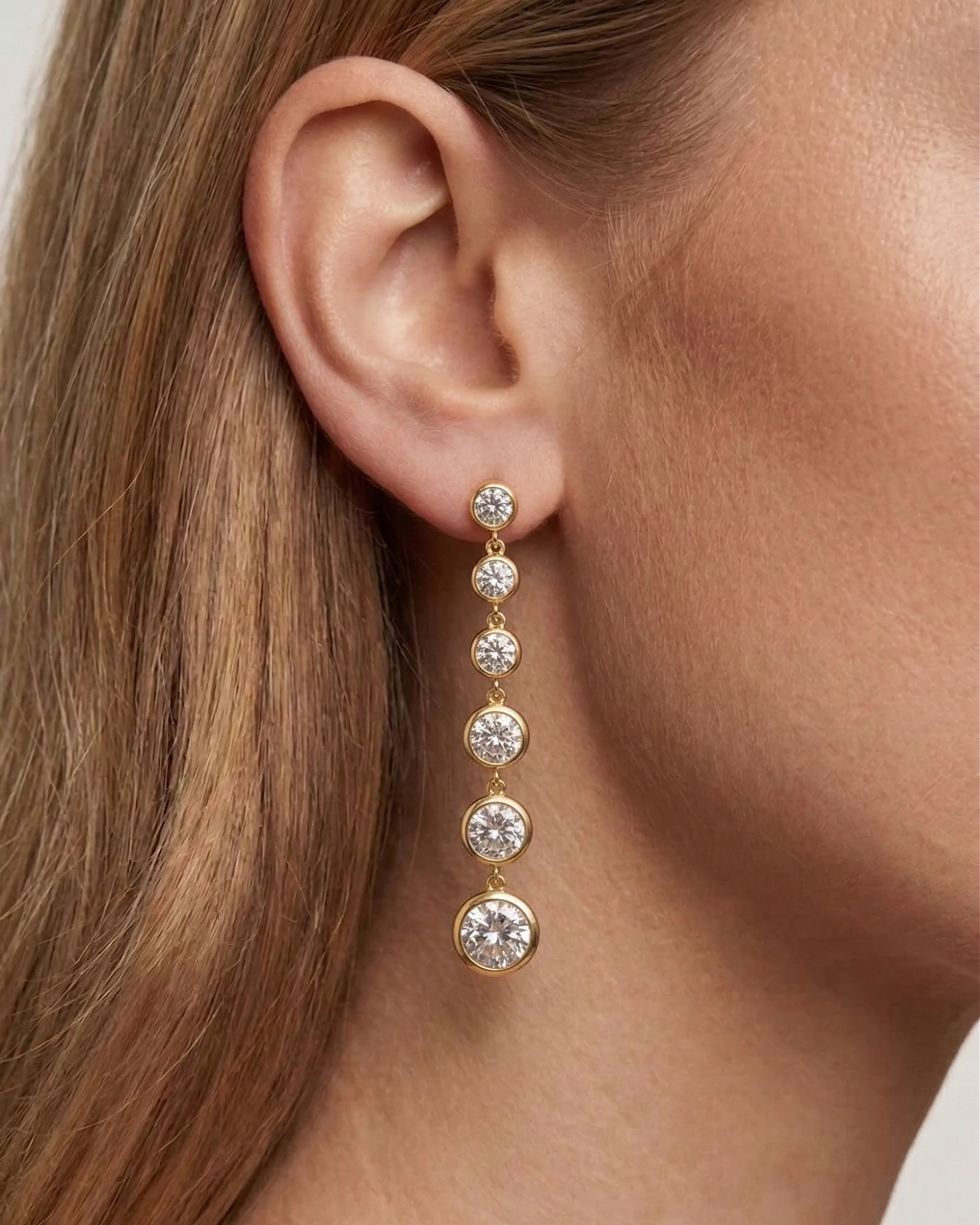 Gold earrings with clear stones worn by a person with brown hair.