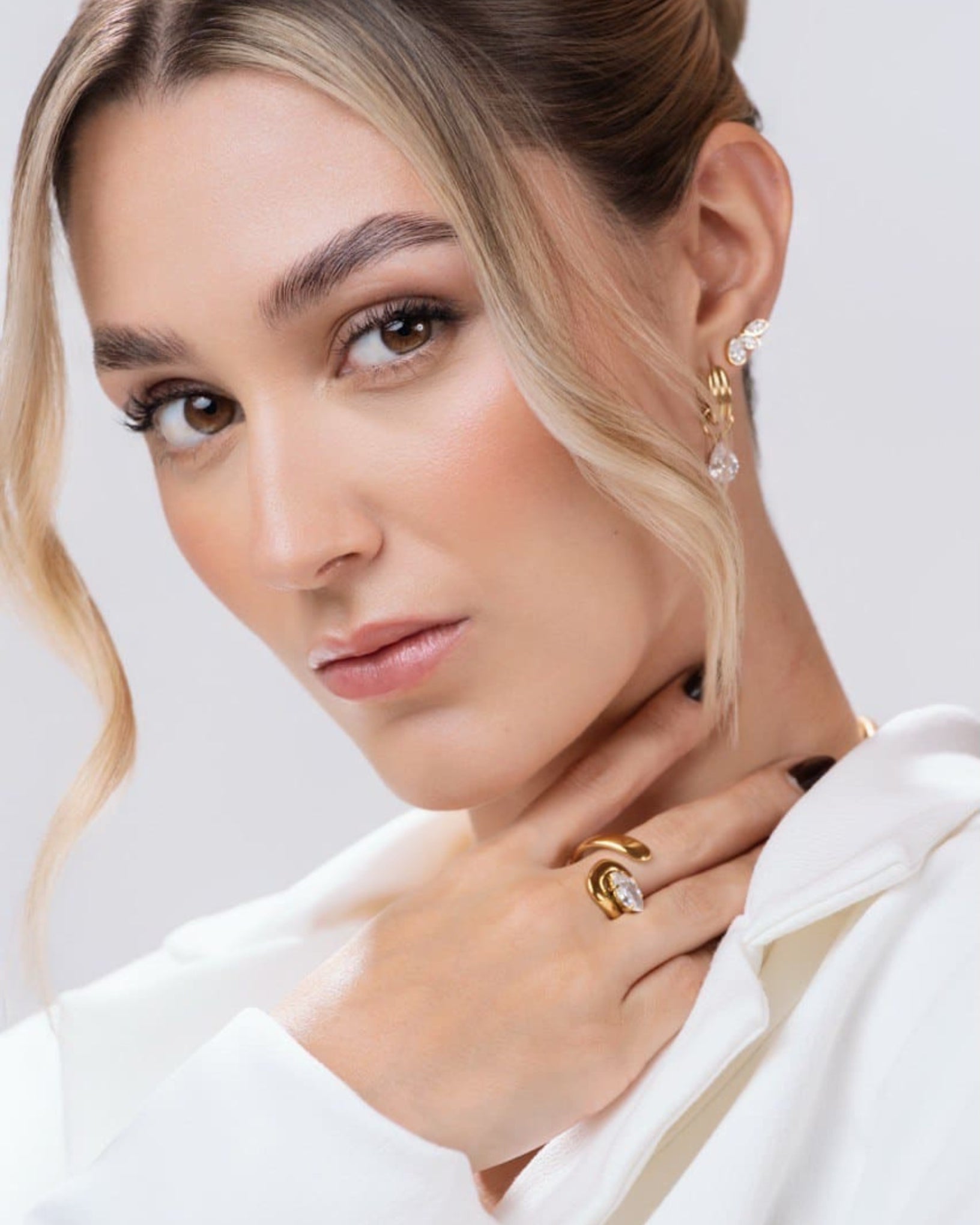 Close-up of a woman wearing gold earrings and ring on a light background