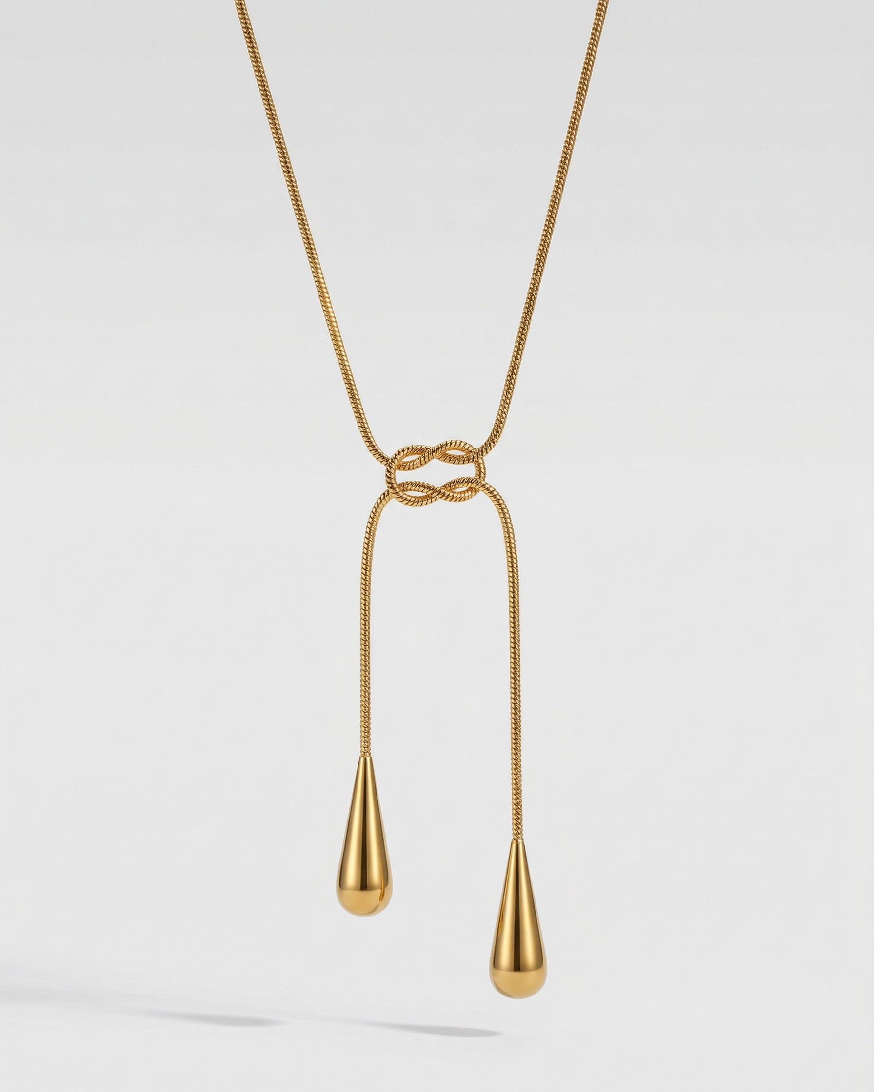 Gold necklace with a knot design and two dangling teardrop pendants on a light gray background
