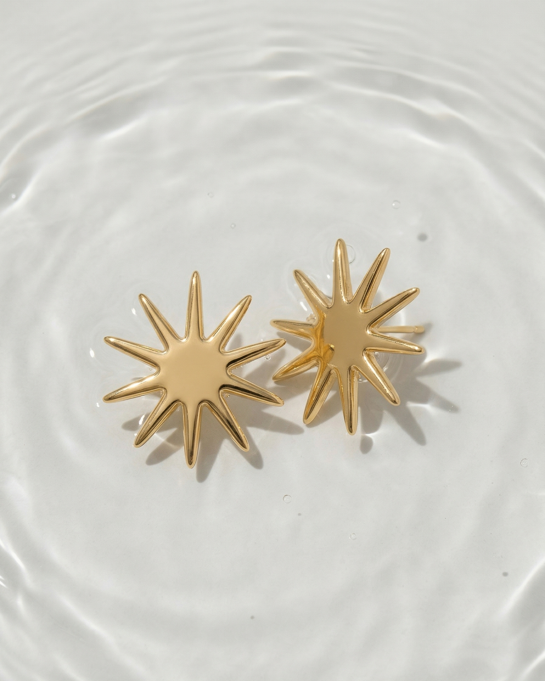 Gold star-shaped earrings on a white plate with water droplets