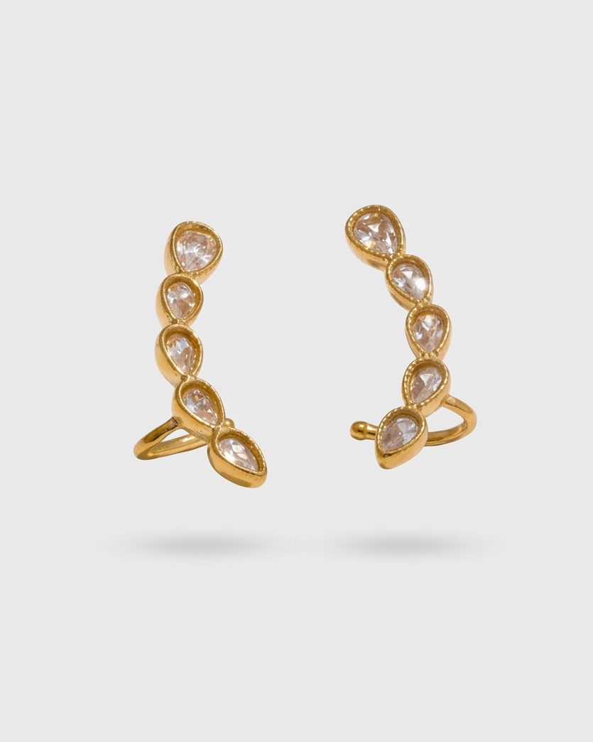 Gold ear cuffs with clear gemstones on a light gray background