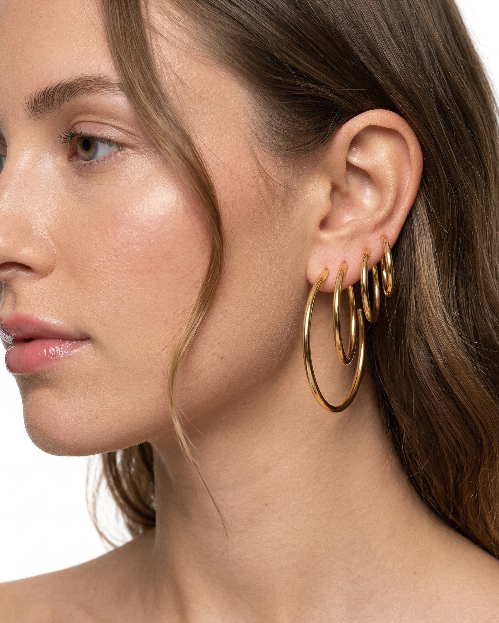 Close-up of a woman wearing gold hoop earrings on a white background