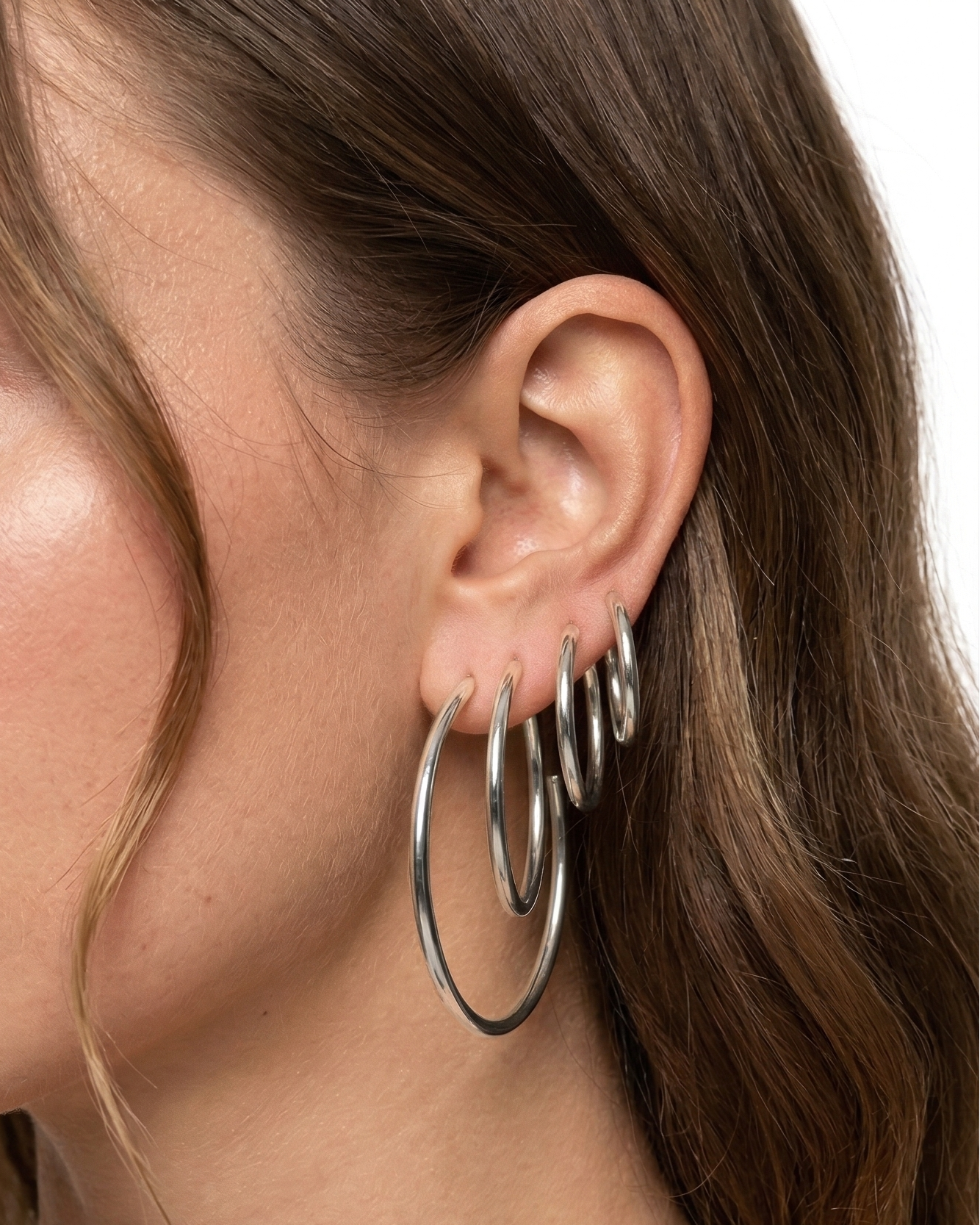 Close-up of a woman wearing silver hoop earrings on a neutral background