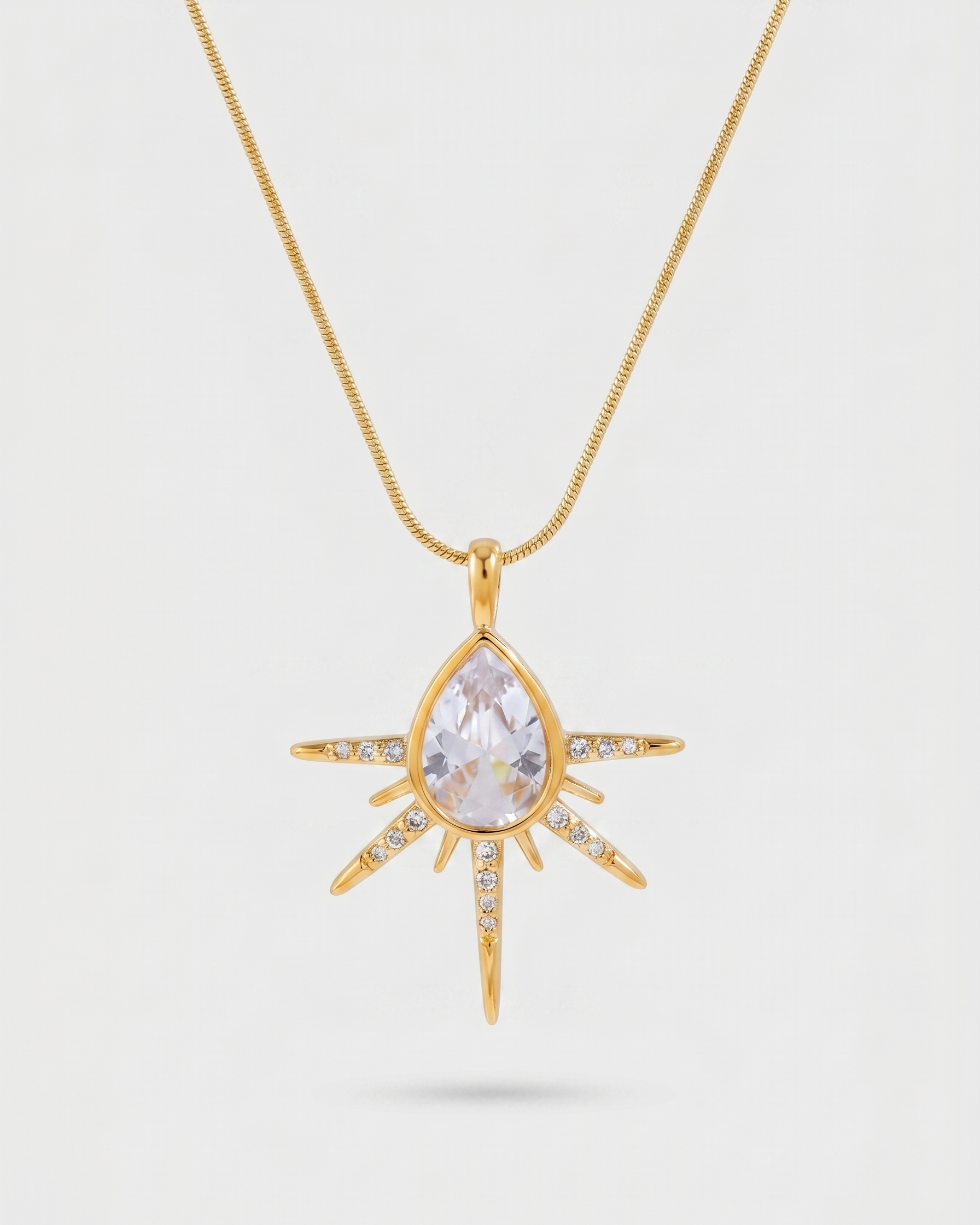 Gold necklace with a teardrop-shaped pendant on a light gray background