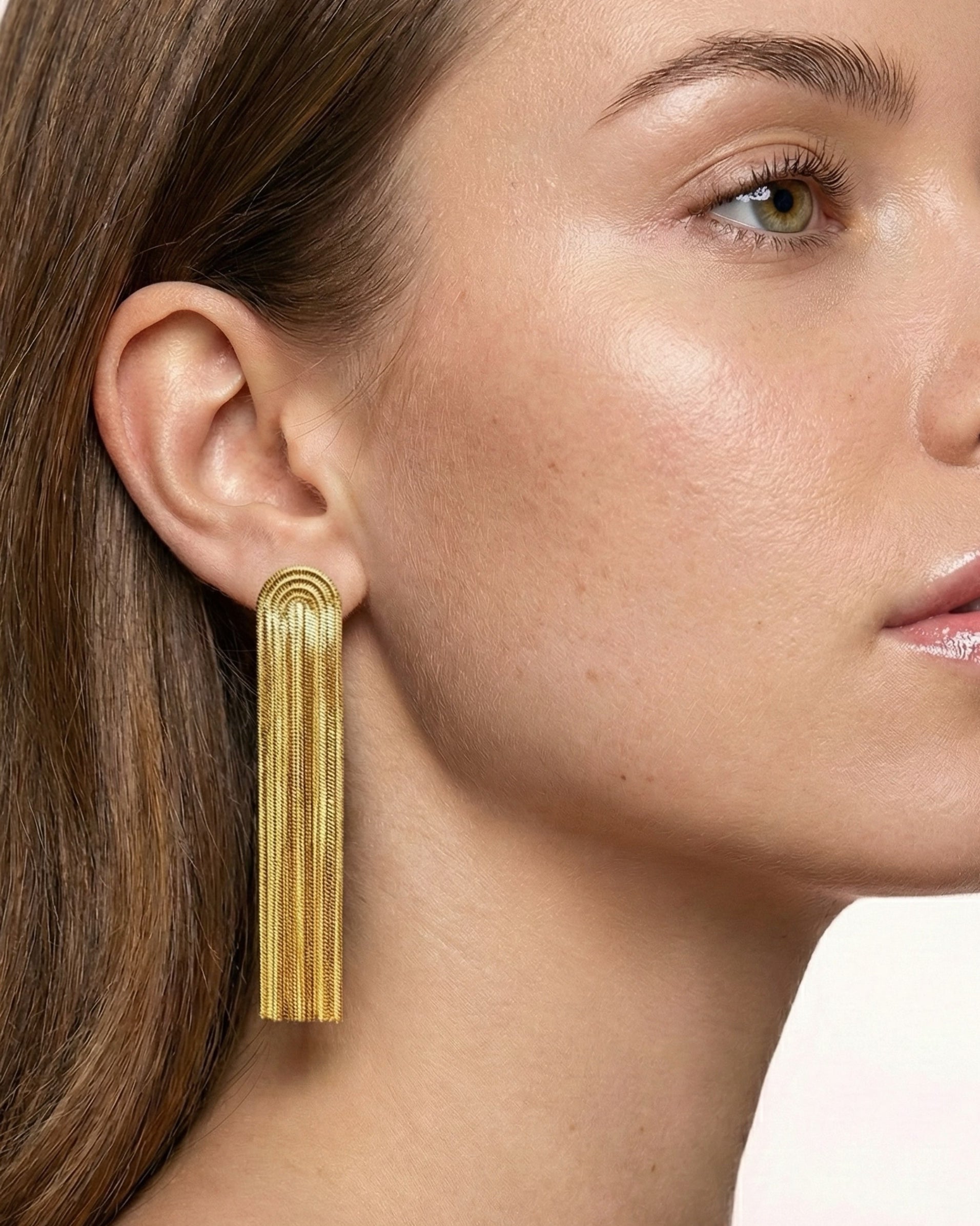 Gold fringe earring worn by a model with a neutral background