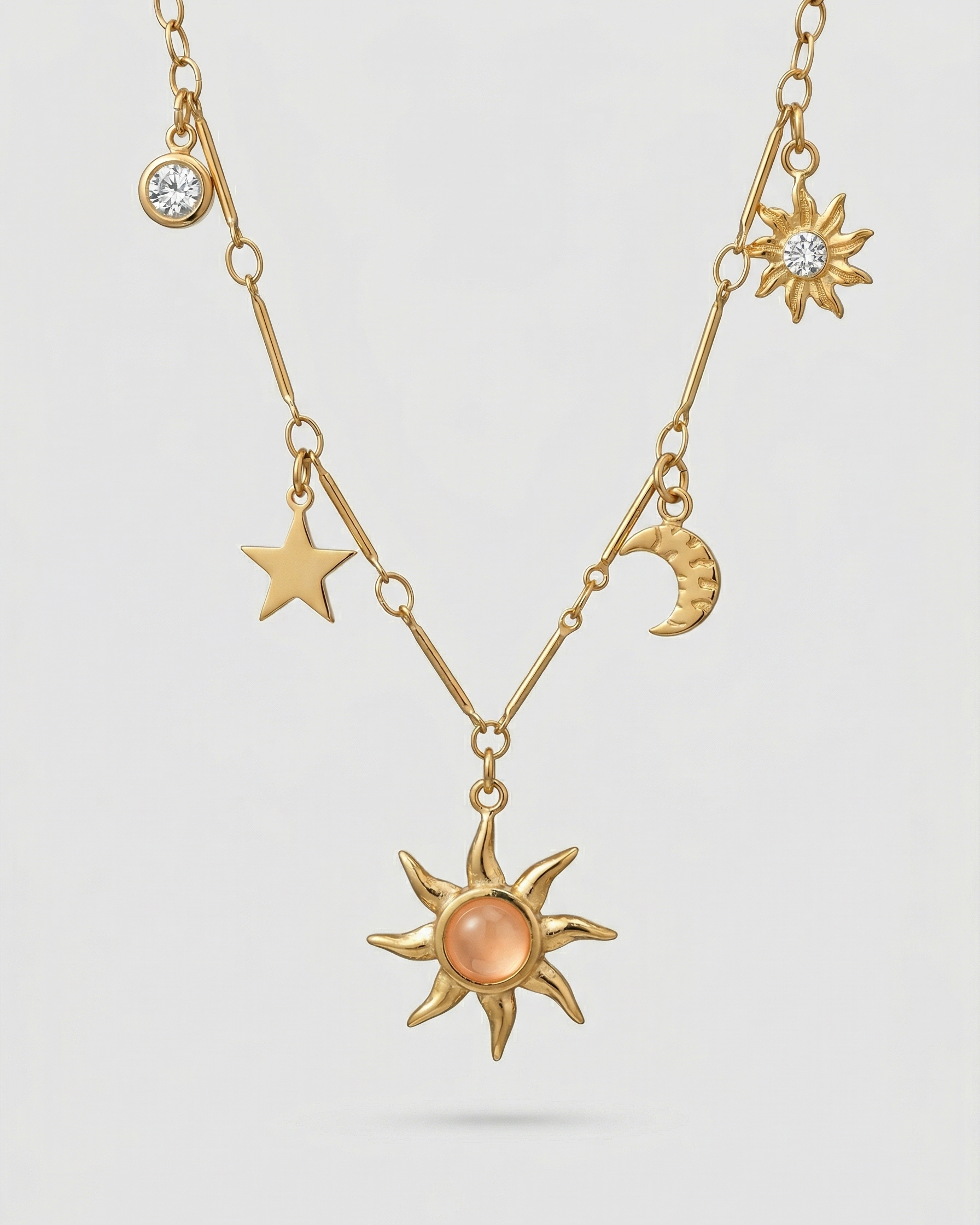 Gold necklace with celestial charms on a light gray background