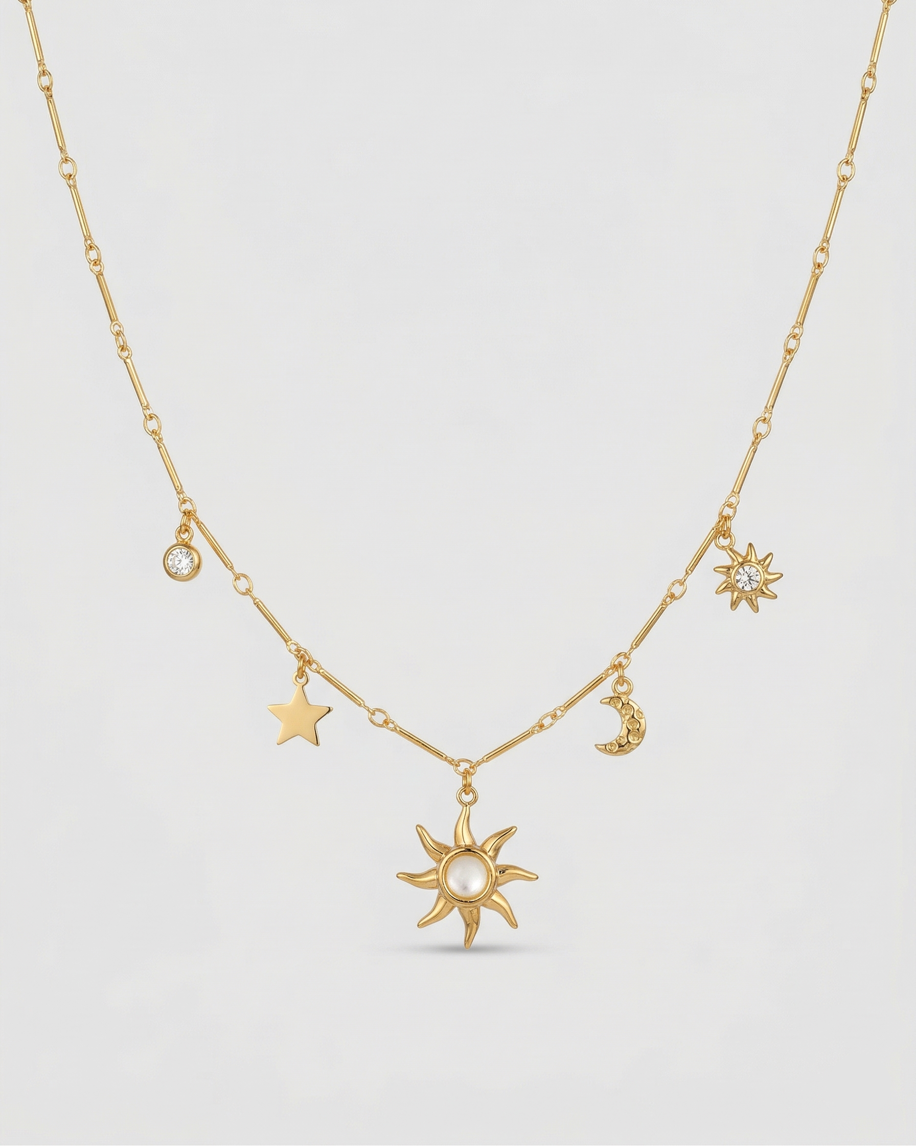 Gold necklace with star, moon, and sun pendants on a light gray background