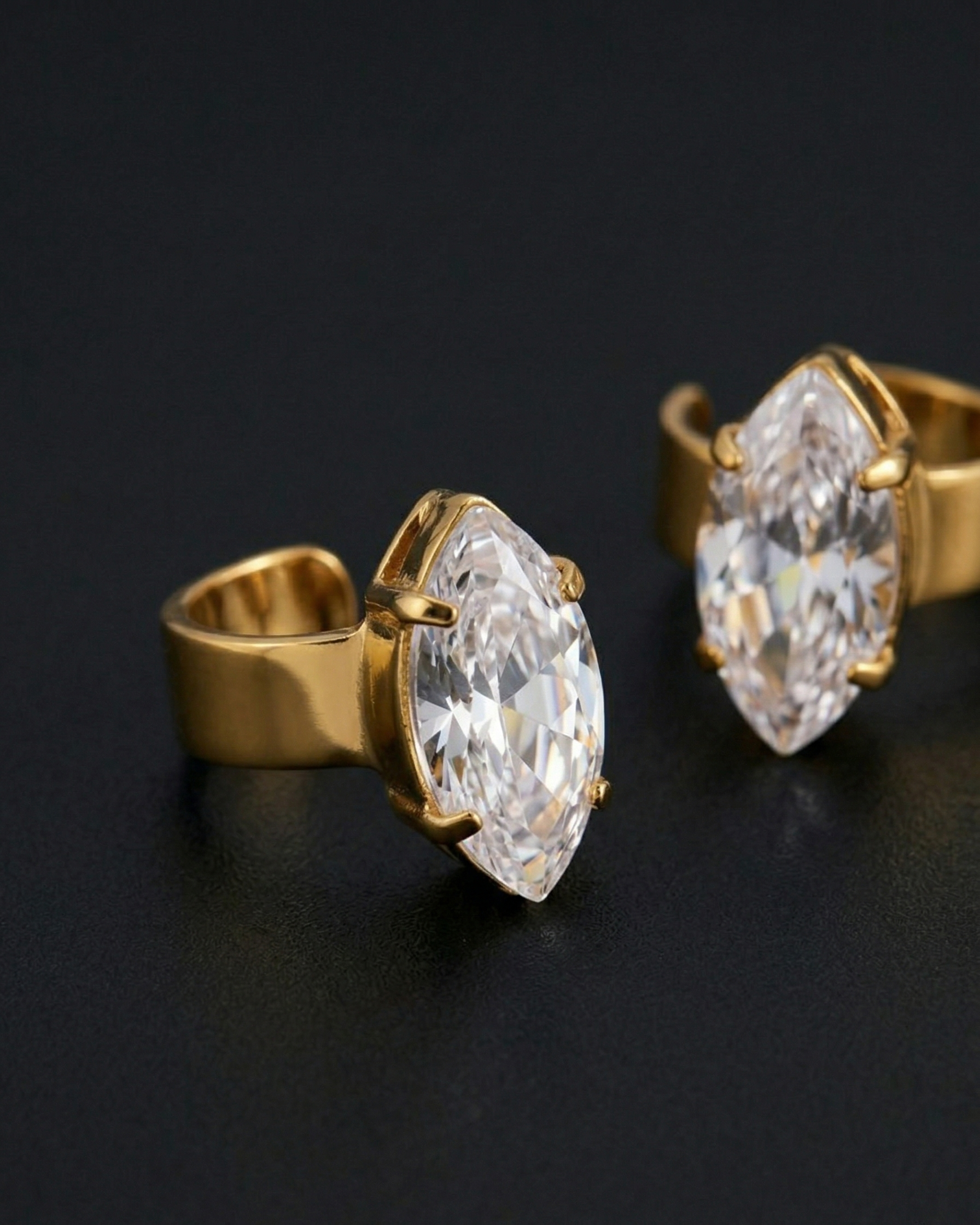 Gold earrings with large clear gemstones on a black background