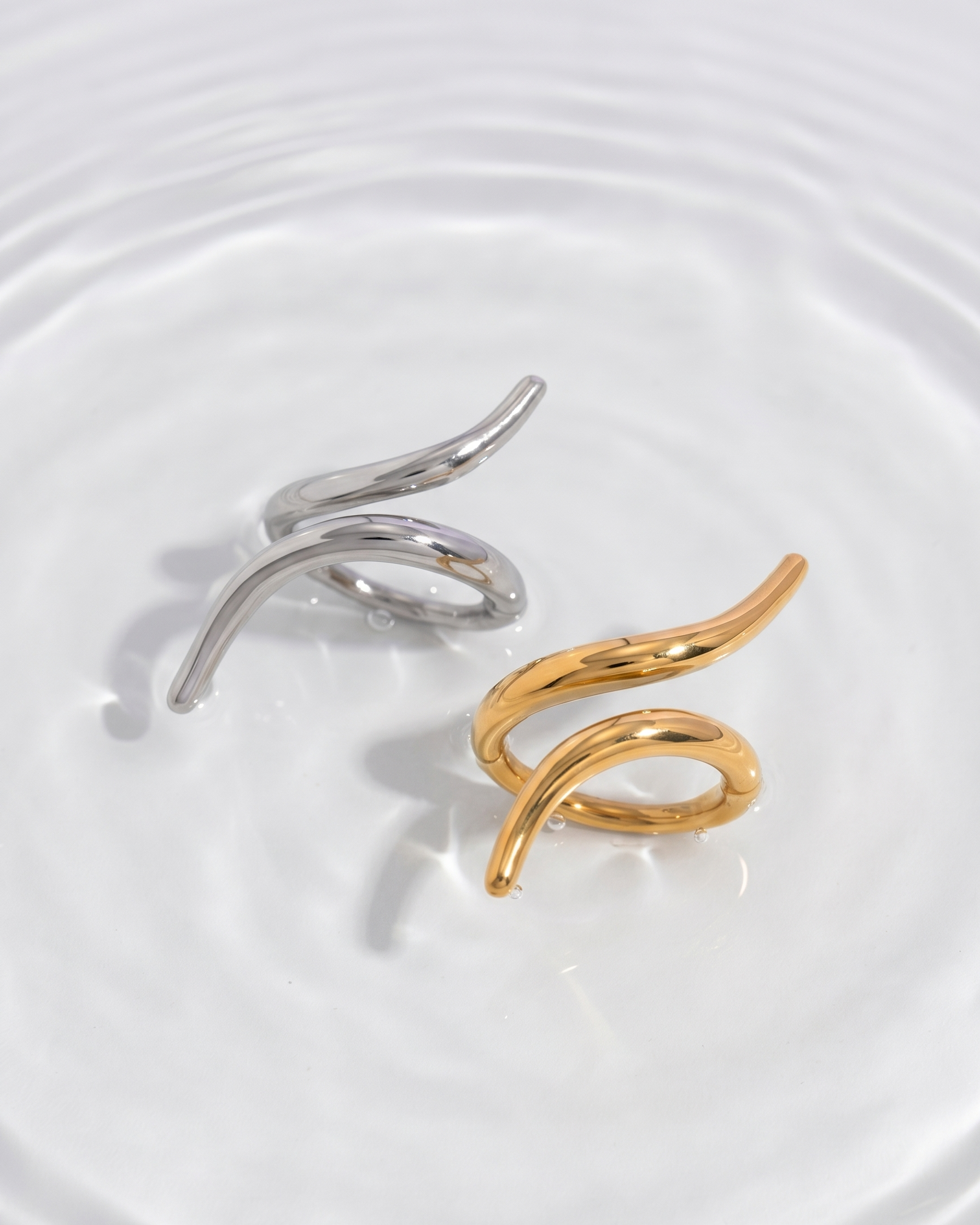 Two gold and silver rings on a white plate with water droplets.