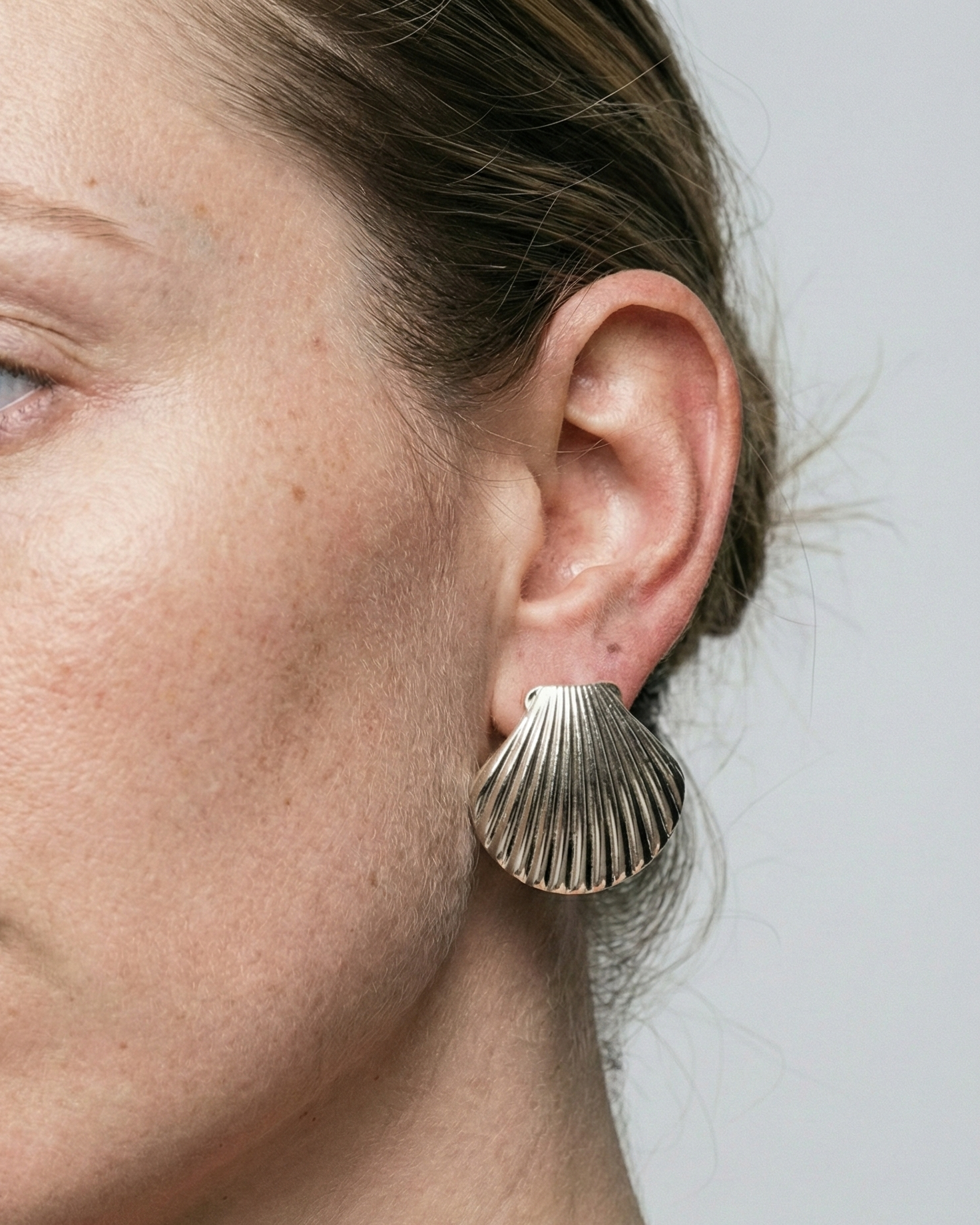Close-up of a person wearing a shell-shaped earring against a neutral background