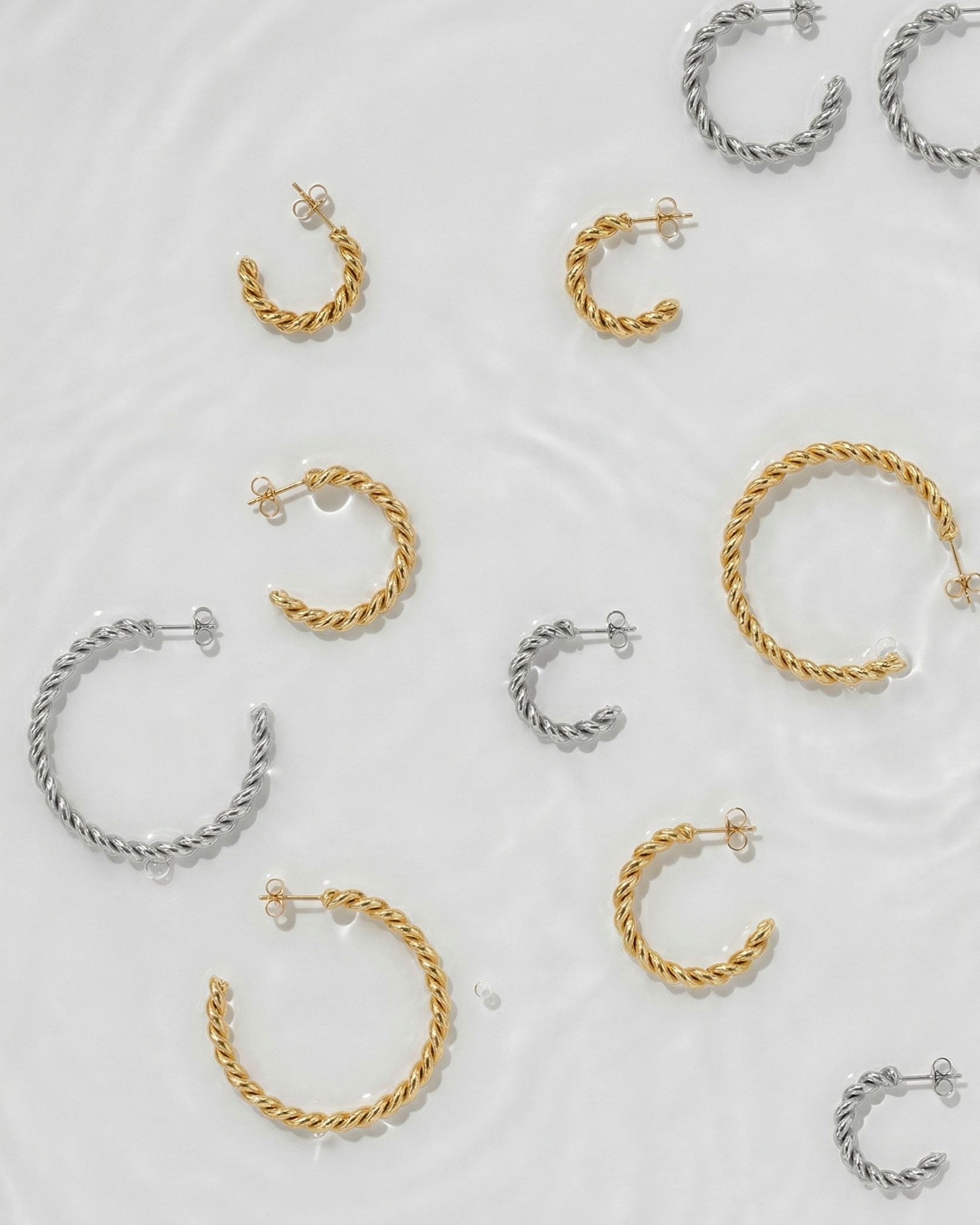Collection of gold and silver hoop earrings on a light gray background