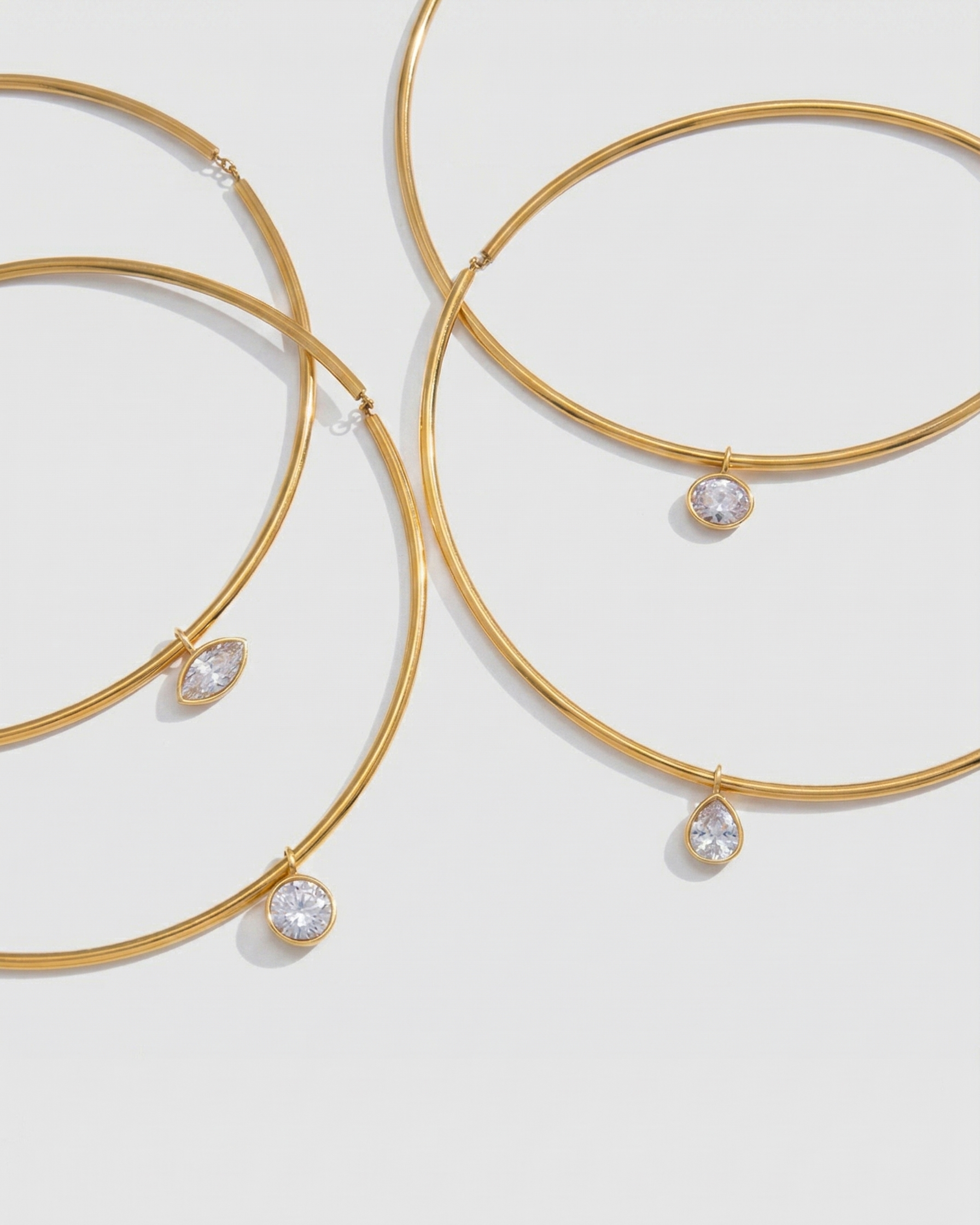 Gold bangles with teardrop-shaped crystals on a light gray background