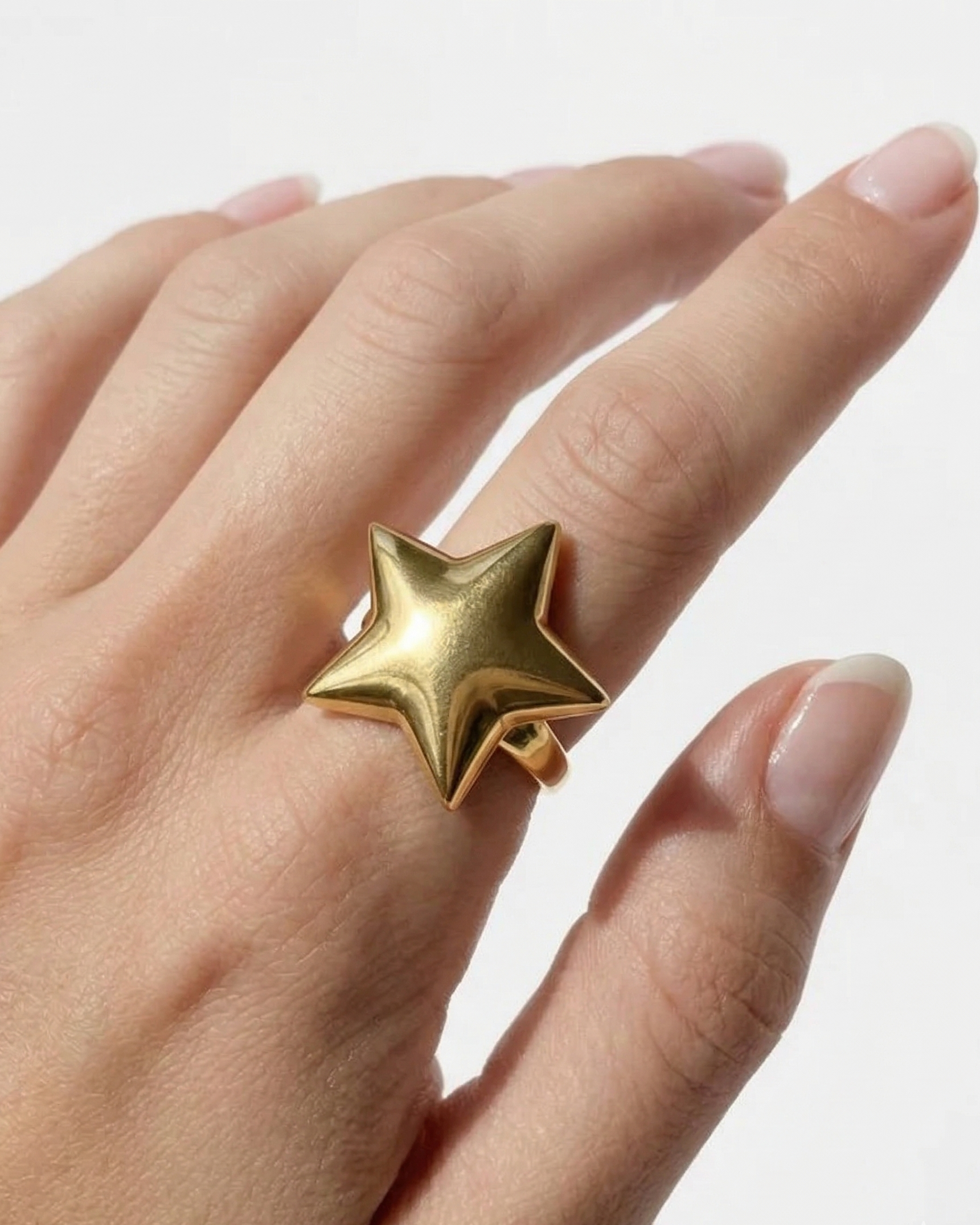 Gold star-shaped ring on a hand against a white background