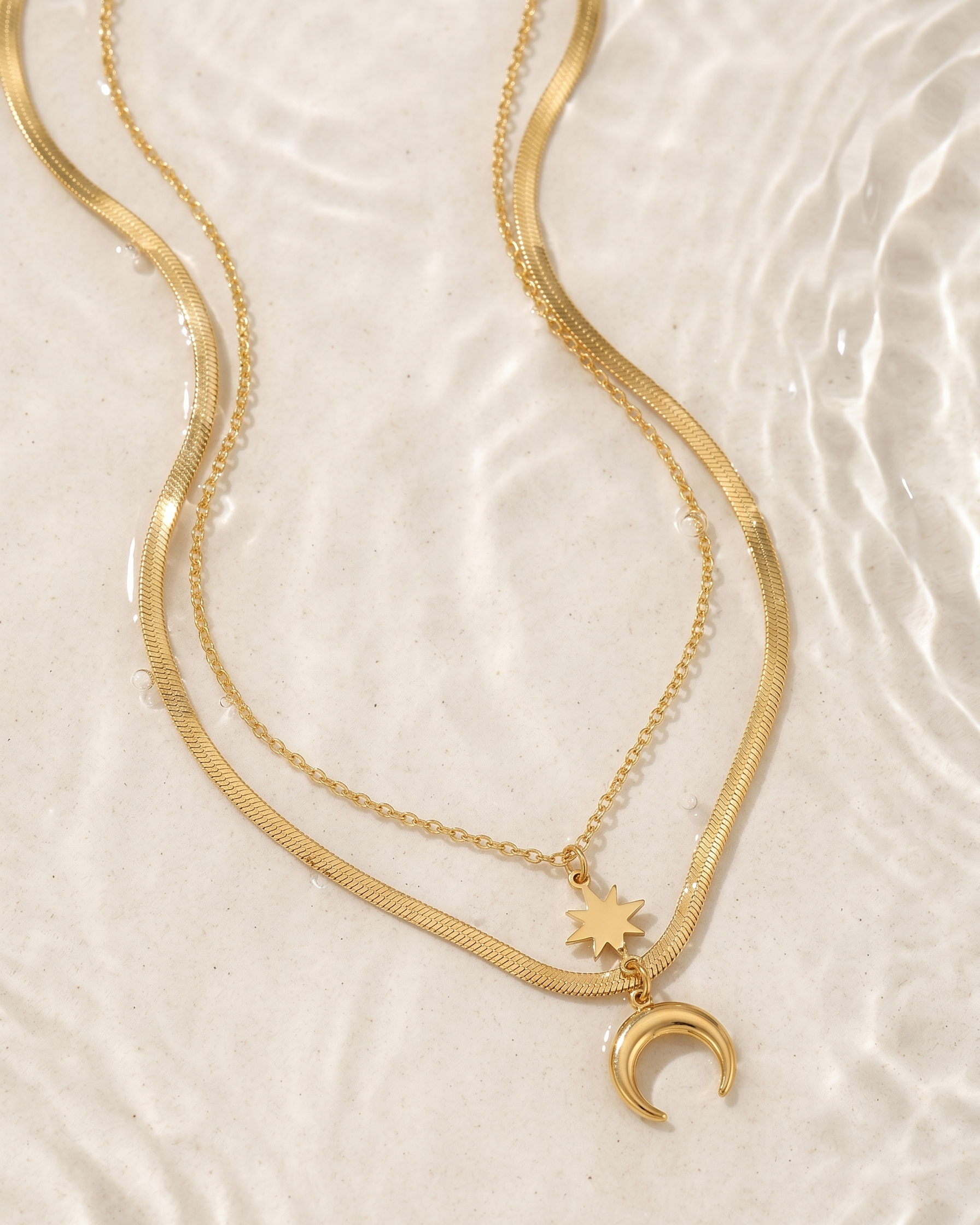 Gold necklaces with star and moon pendants on a textured beige surface