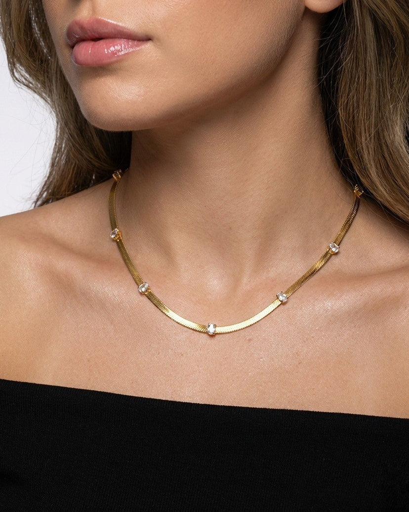 Gold necklace worn by a person against a neutral background