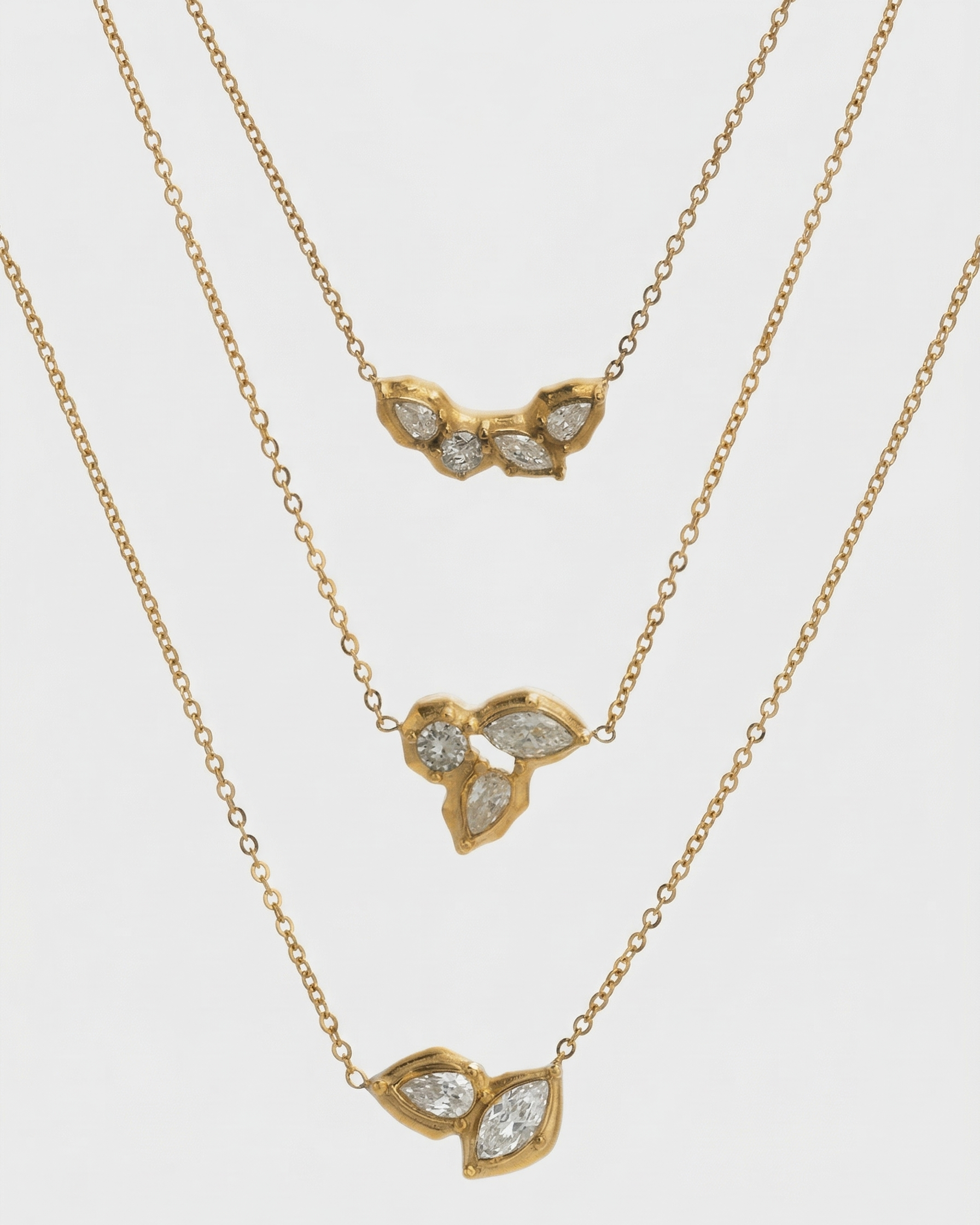 Three gold necklaces with leaf-shaped pendants on a light gray background