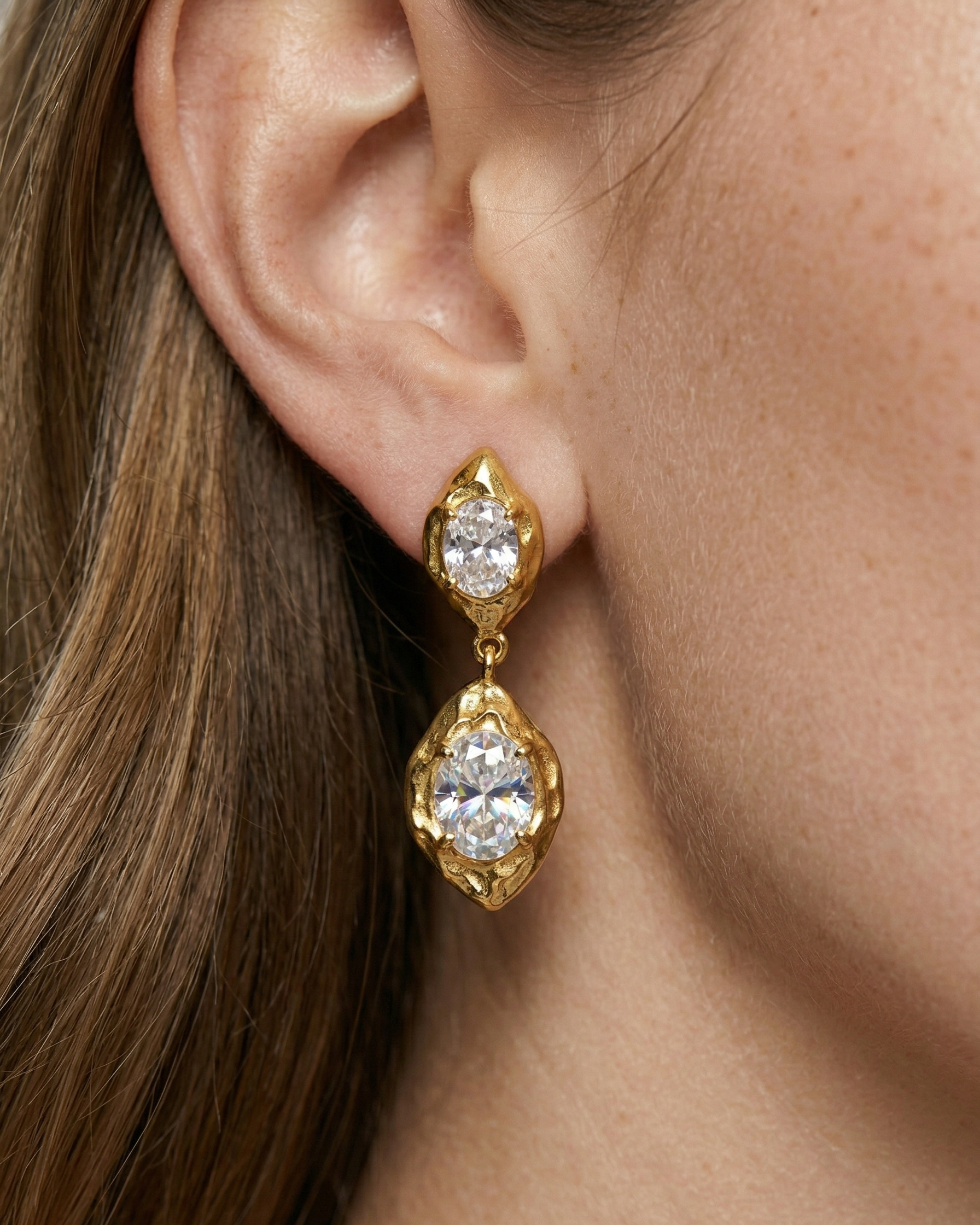 Gold earrings with clear gemstones worn by a person