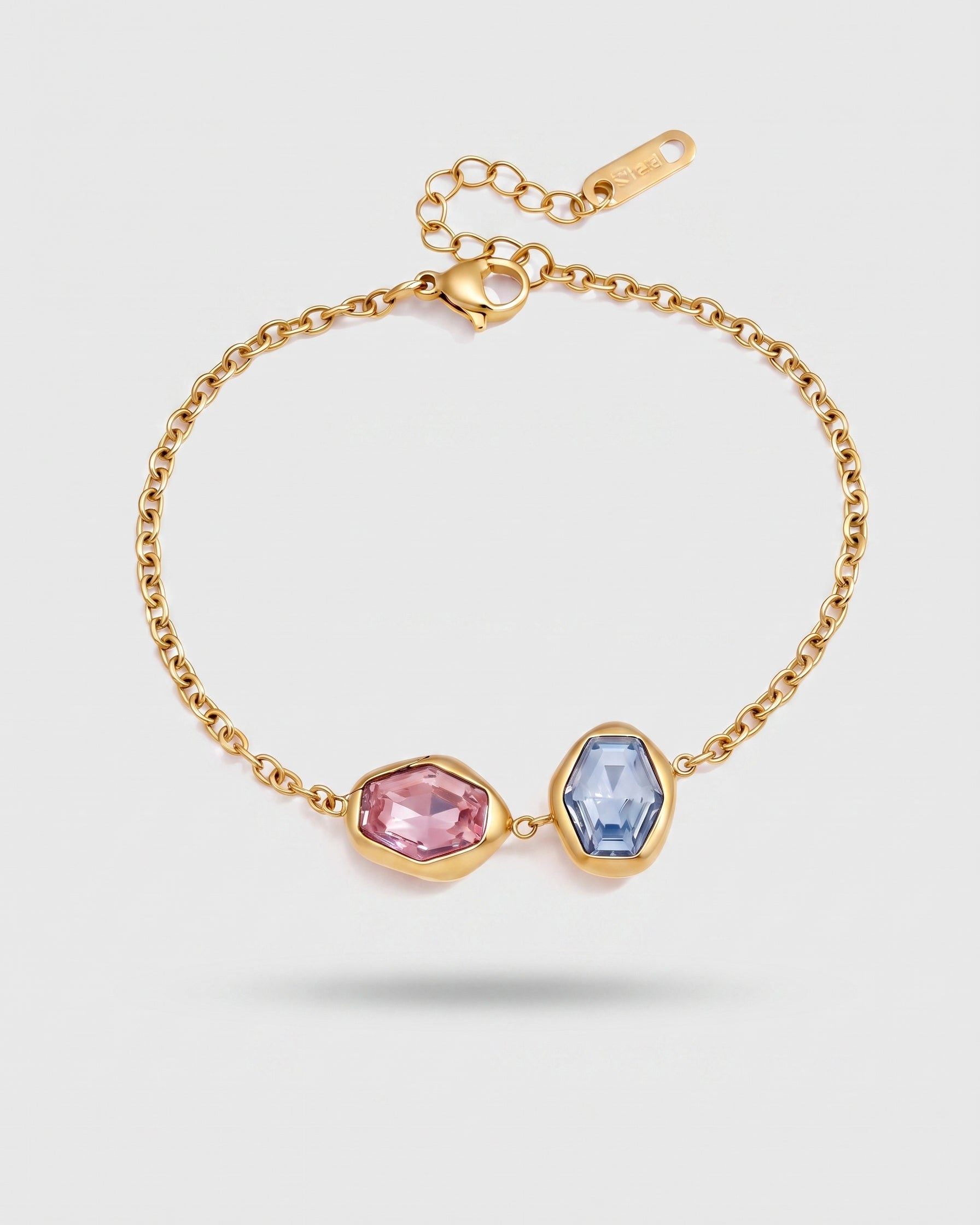 A gold chain bracelet with two faceted gemstone charms, one pink and one light blue, set in gold bezels on a light gray background.