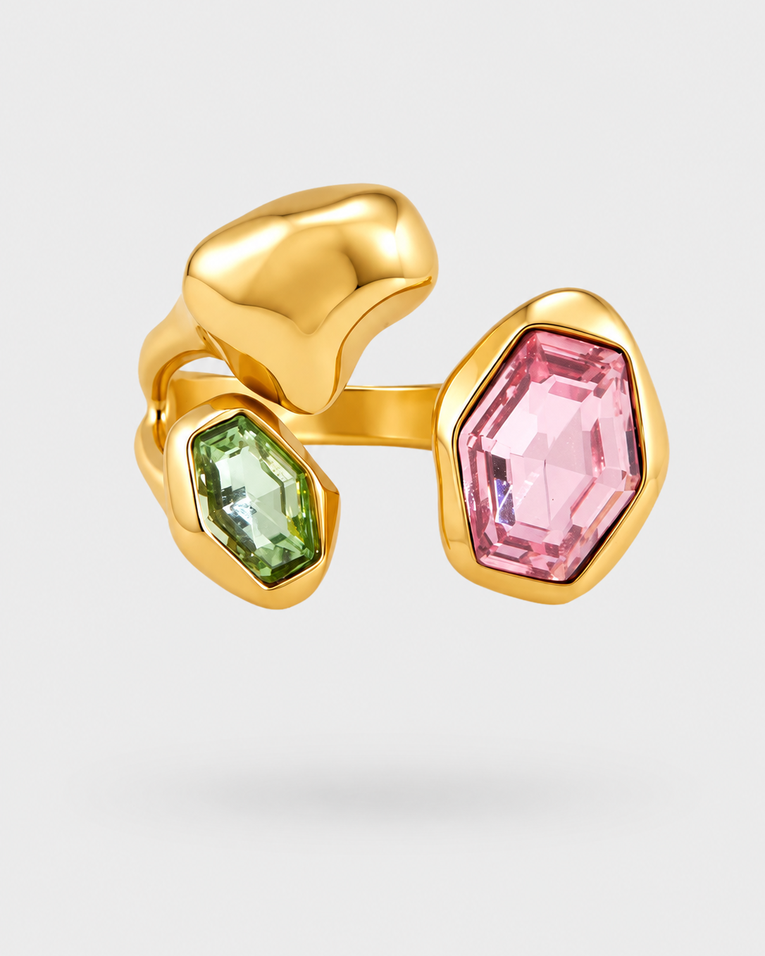 A gold ring featuring two large, organic-shaped bezel settings: one with a faceted light green gemstone and the other with a faceted light pink gemstone, set against a clean light gray background.
