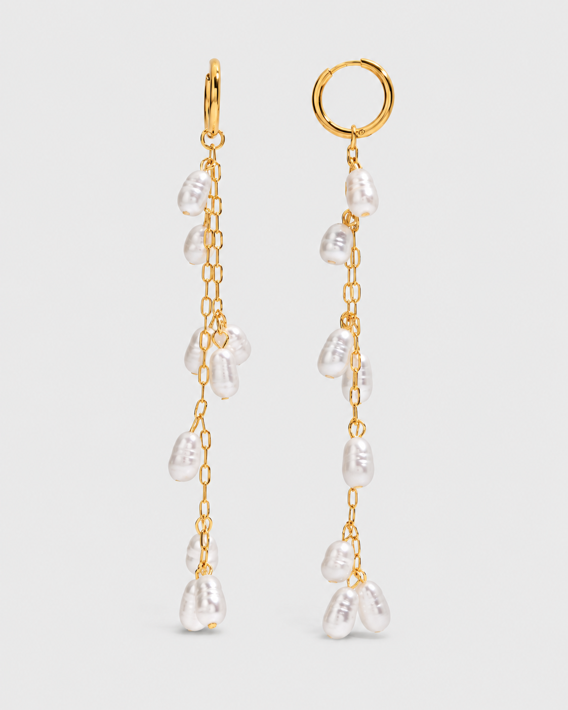 A pair of gold-tone dangle earrings with irregular white baroque pearls suspended on delicate chains, set against a light gray background.