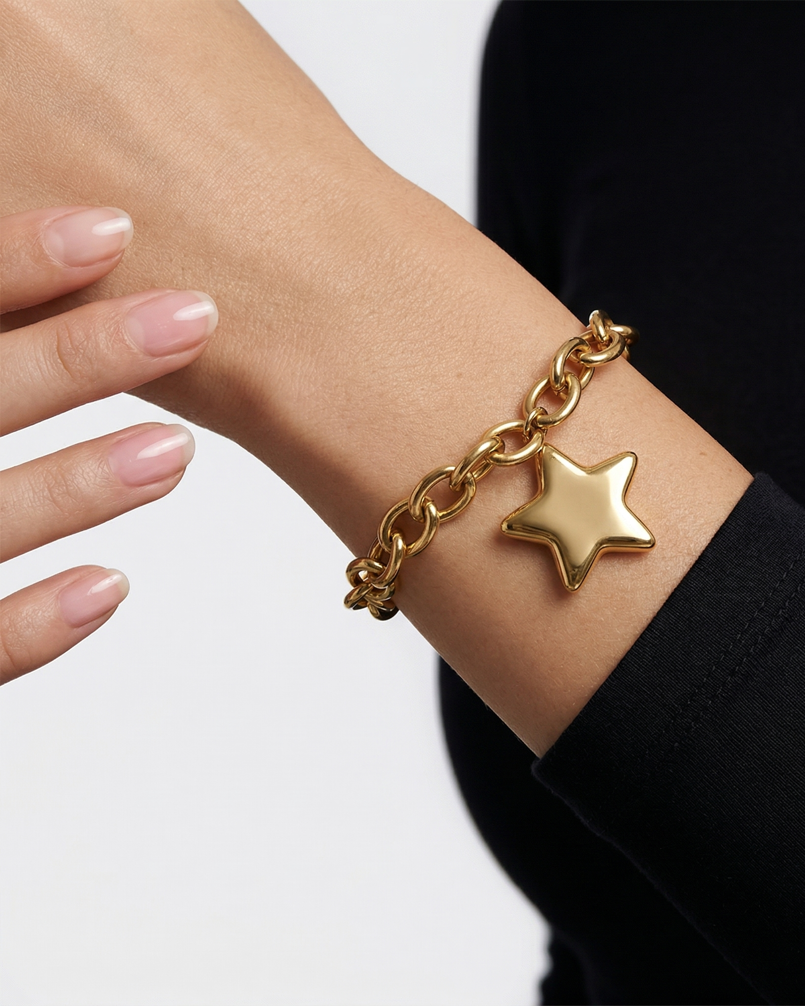 Gold chain bracelet with a star charm on a wrist against a neutral background