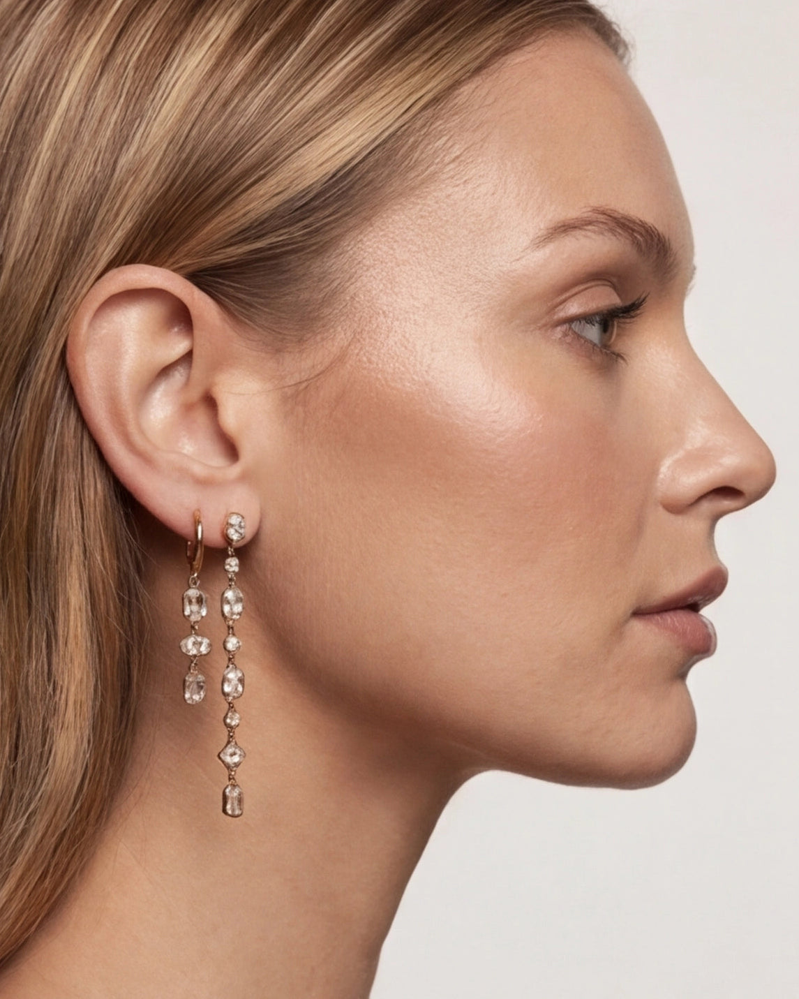 Close-up of a woman wearing a dangling earring with a plain background