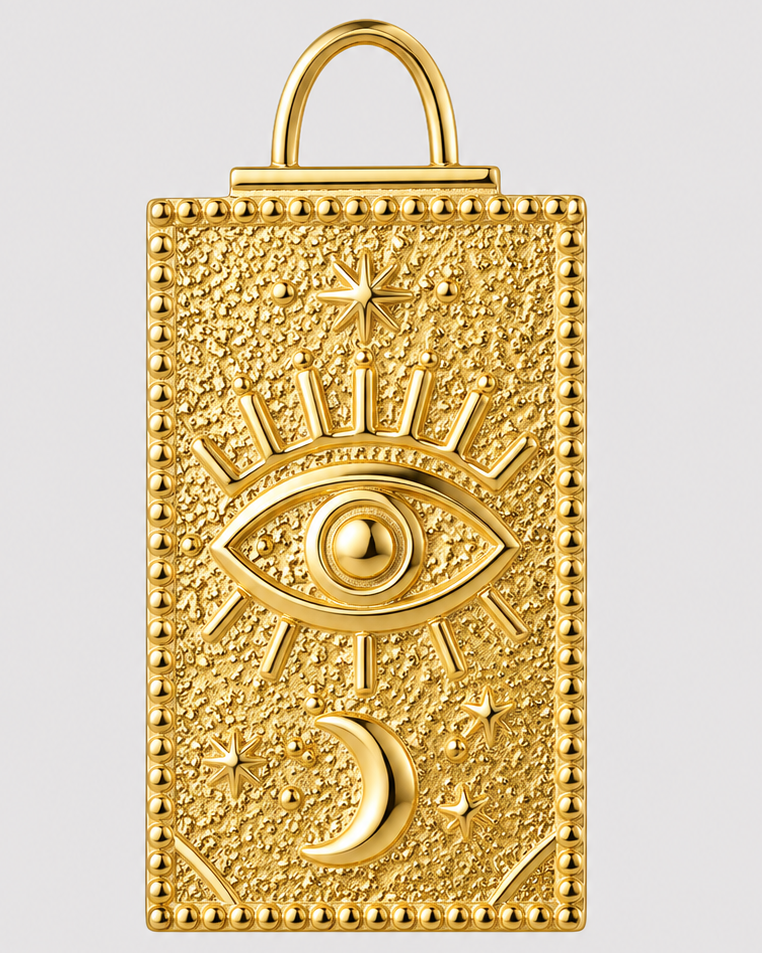 A gold-toned rectangular pendant or charm with a textured surface, featuring an eye of providence design, a crescent moon, stars, and a top loop, shown on a light gray background.