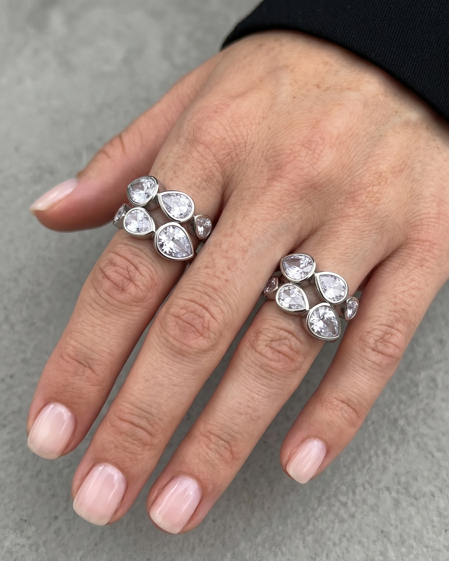 Hand wearing two silver rings with clear gemstones on a gray background