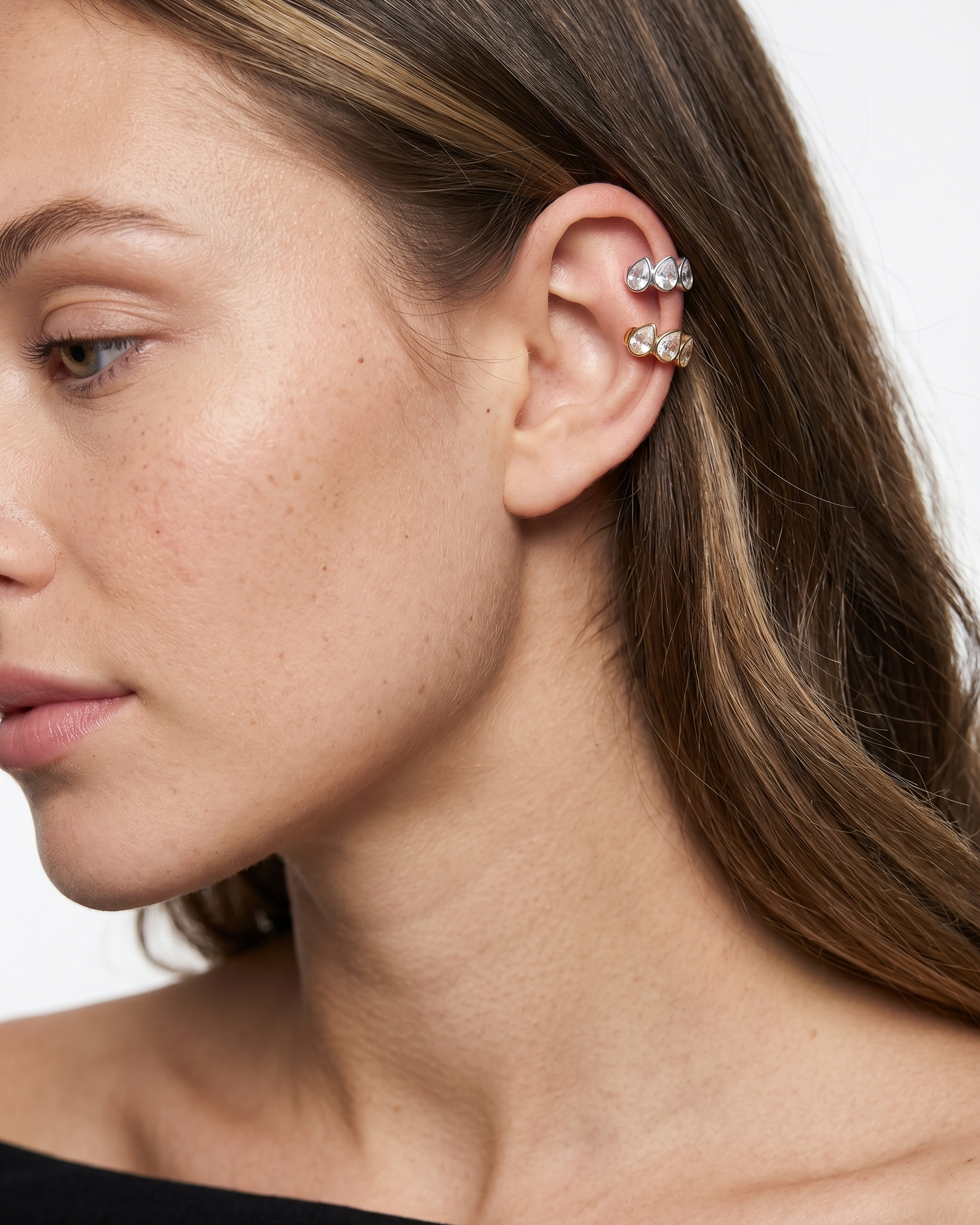 Close-up of a woman's ear with multiple earrings on a neutral background
